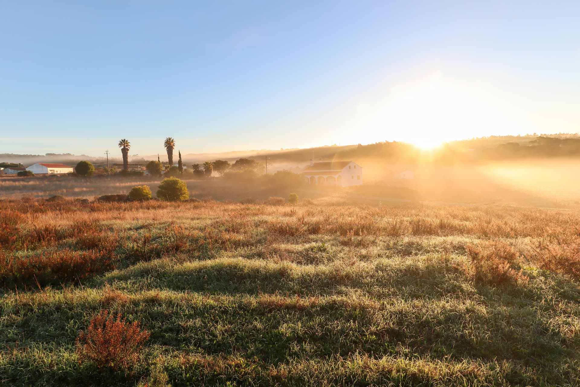 Alentejo landscape with village in morning fog, rising sun over grassy fields at Rota Vicentina.
