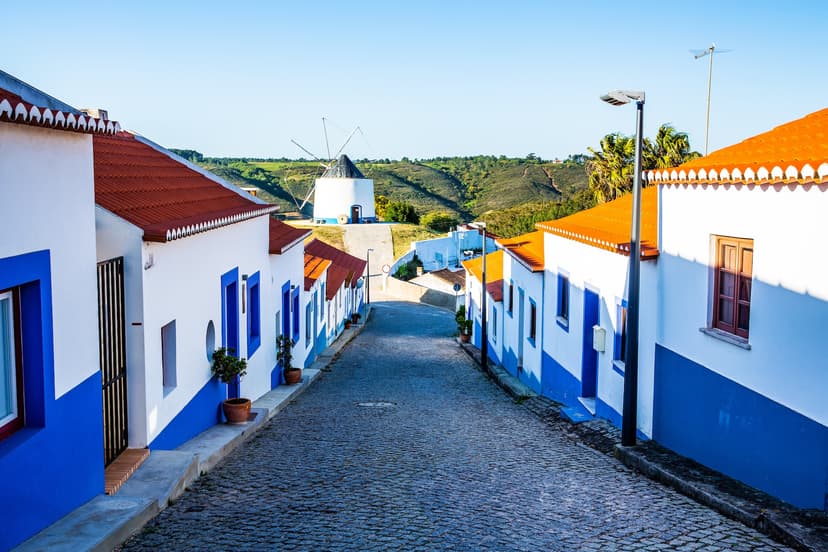 Cobblestone street in Odeceixe, Portugal, lined with white and blue houses leading to a traditional windmill.