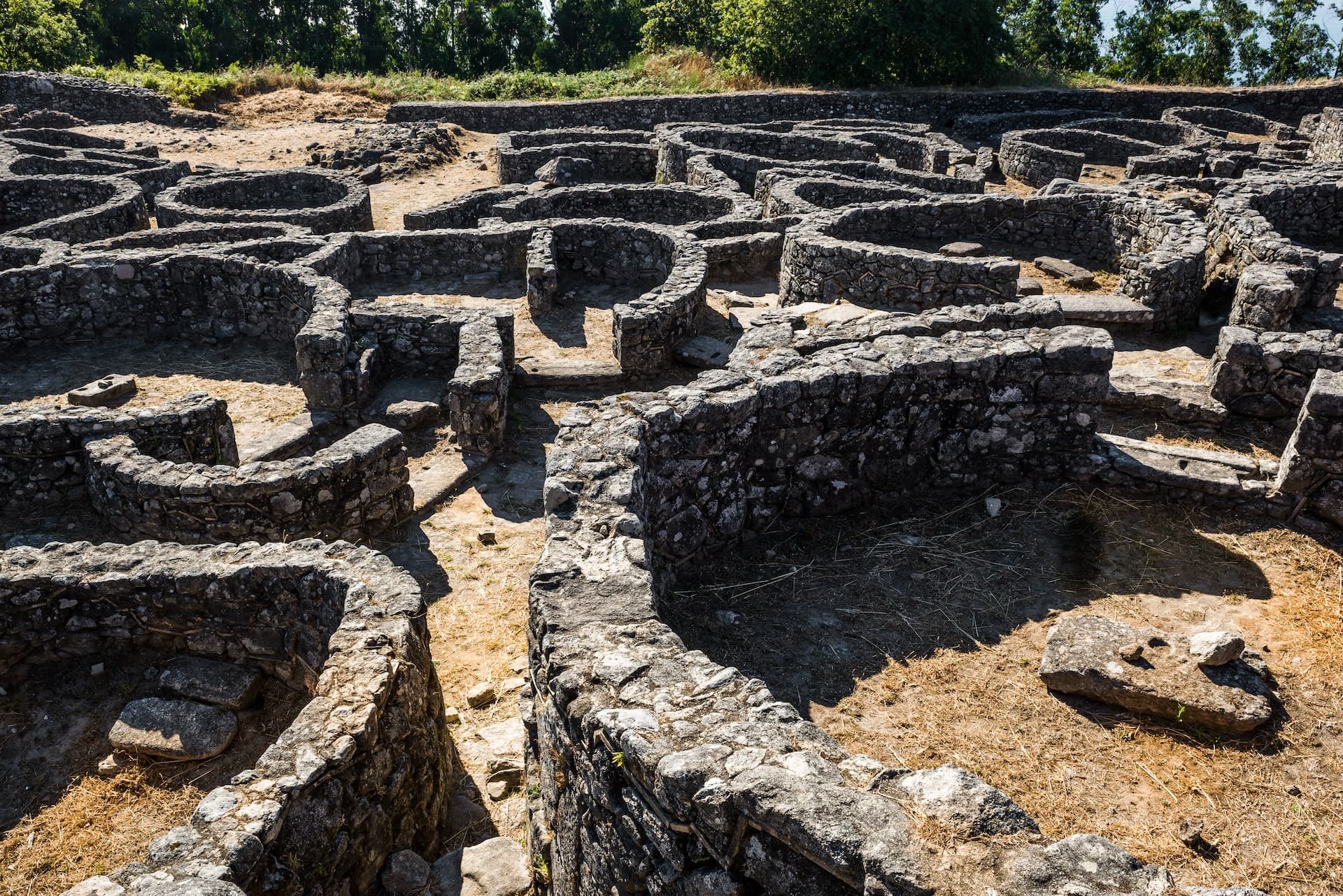 Circular stone ruins of Castro de Santa Tegra in Pontevedra, Spain, under sunny sky.