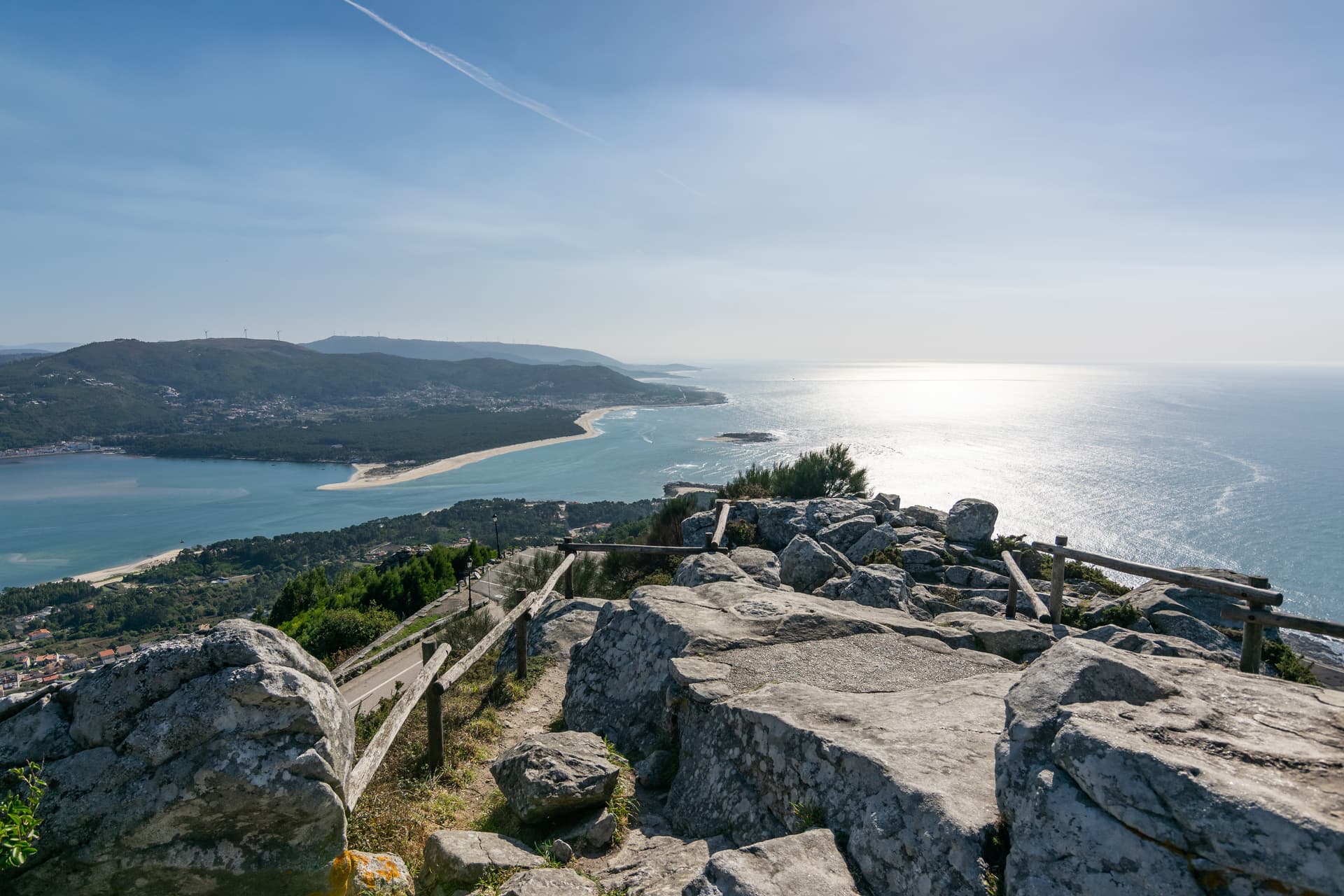 Rocky viewpoint overlooking A Guarda estuary and the Atlantic Ocean under a bright sky.