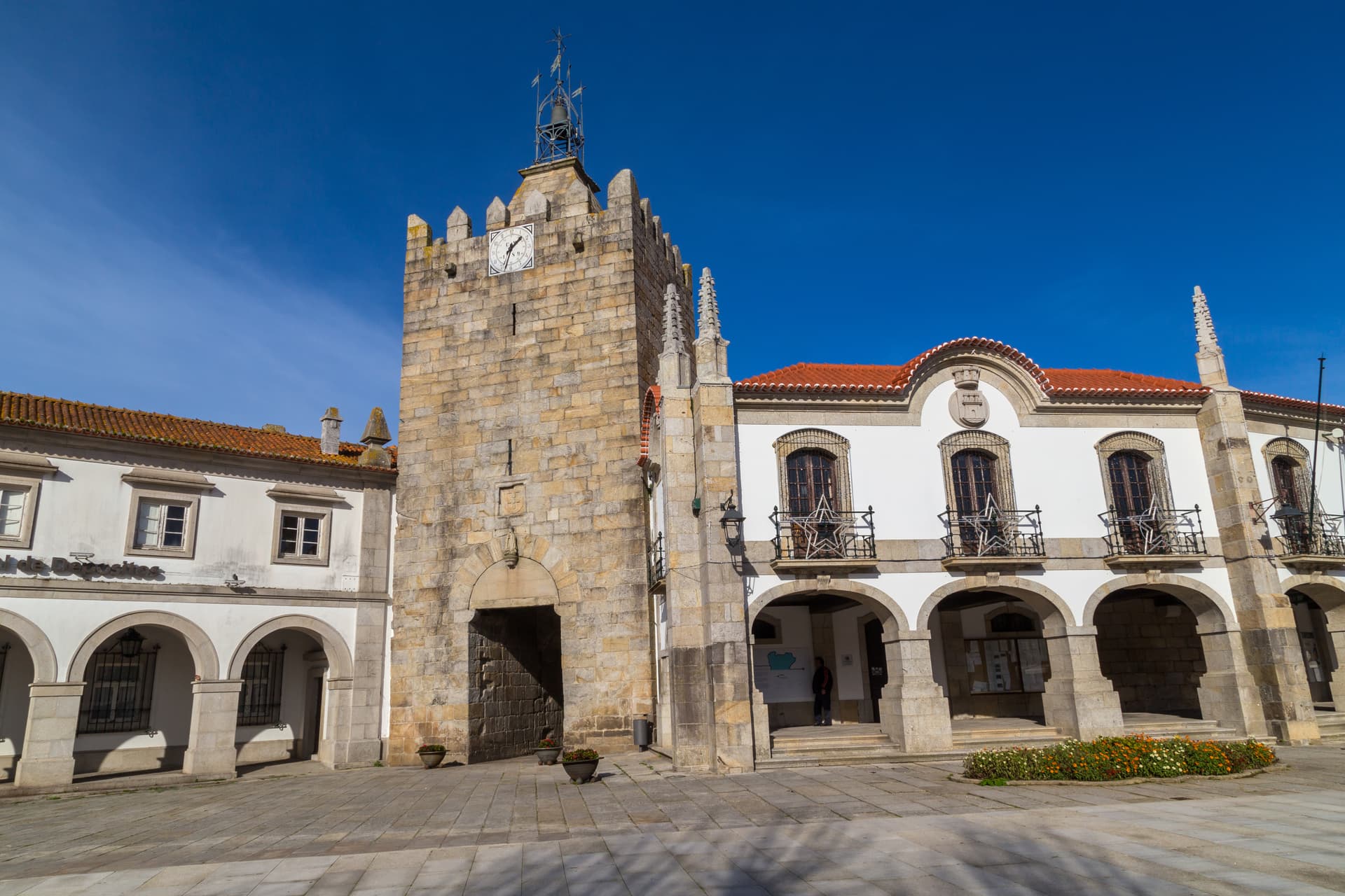 Caminha City Hall with stone clock tower and arched portico under bright blue sky.