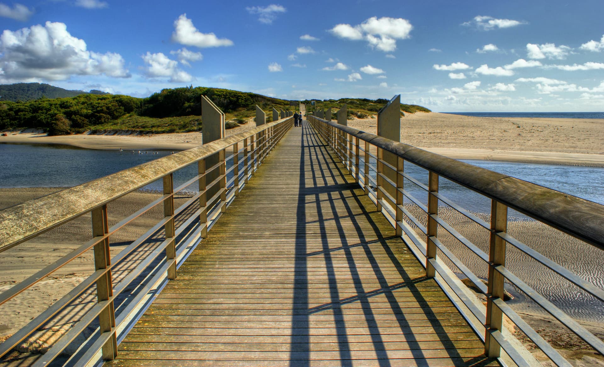 Wooden pedestrian bridge over water channel near sandy beach in Vila Praia de Âncora, Portugal.