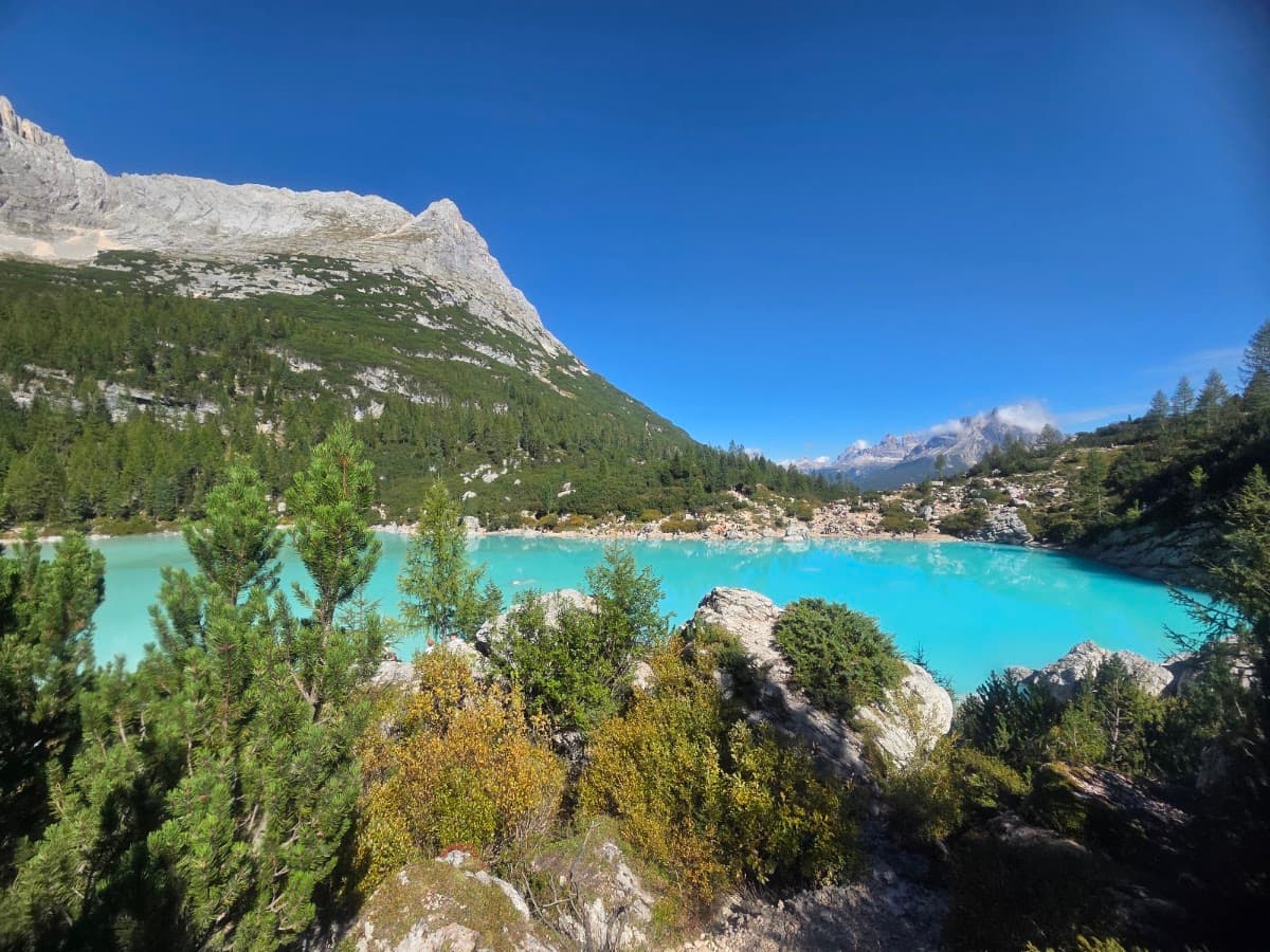 Turquoise alpine lake with rocky shore and surrounding mountains under blue sky