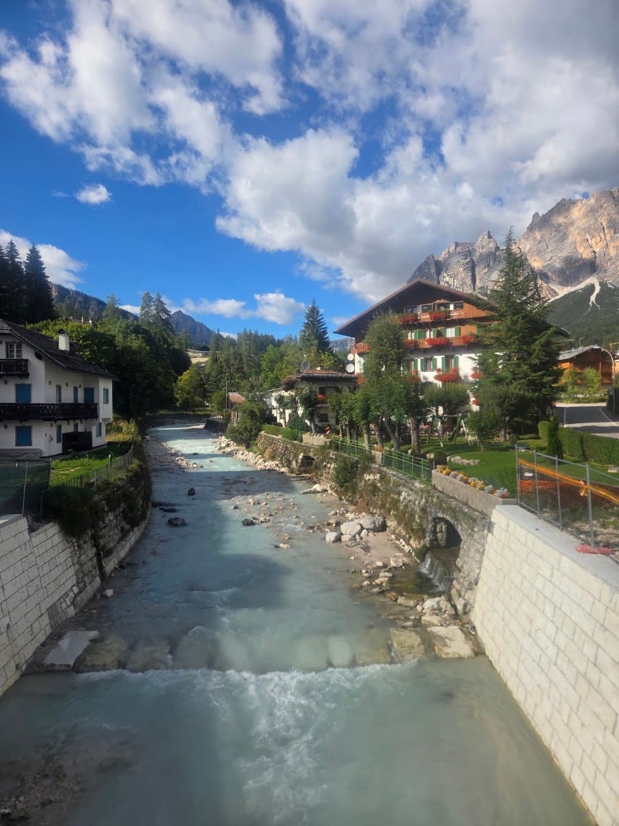 Alpine river flowing through mountain village with traditional houses under cloudy blue sky