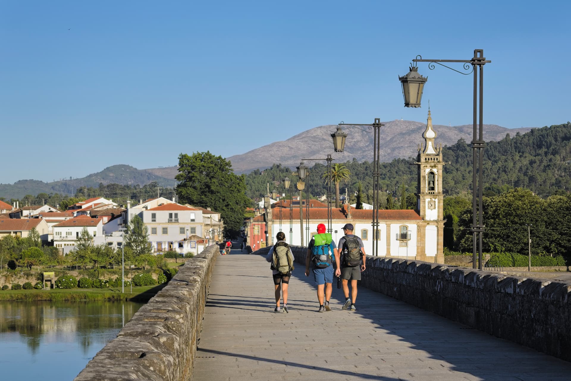 Hikers walking across the Roman bridge in Ponte de Lima toward a town with a church tower.