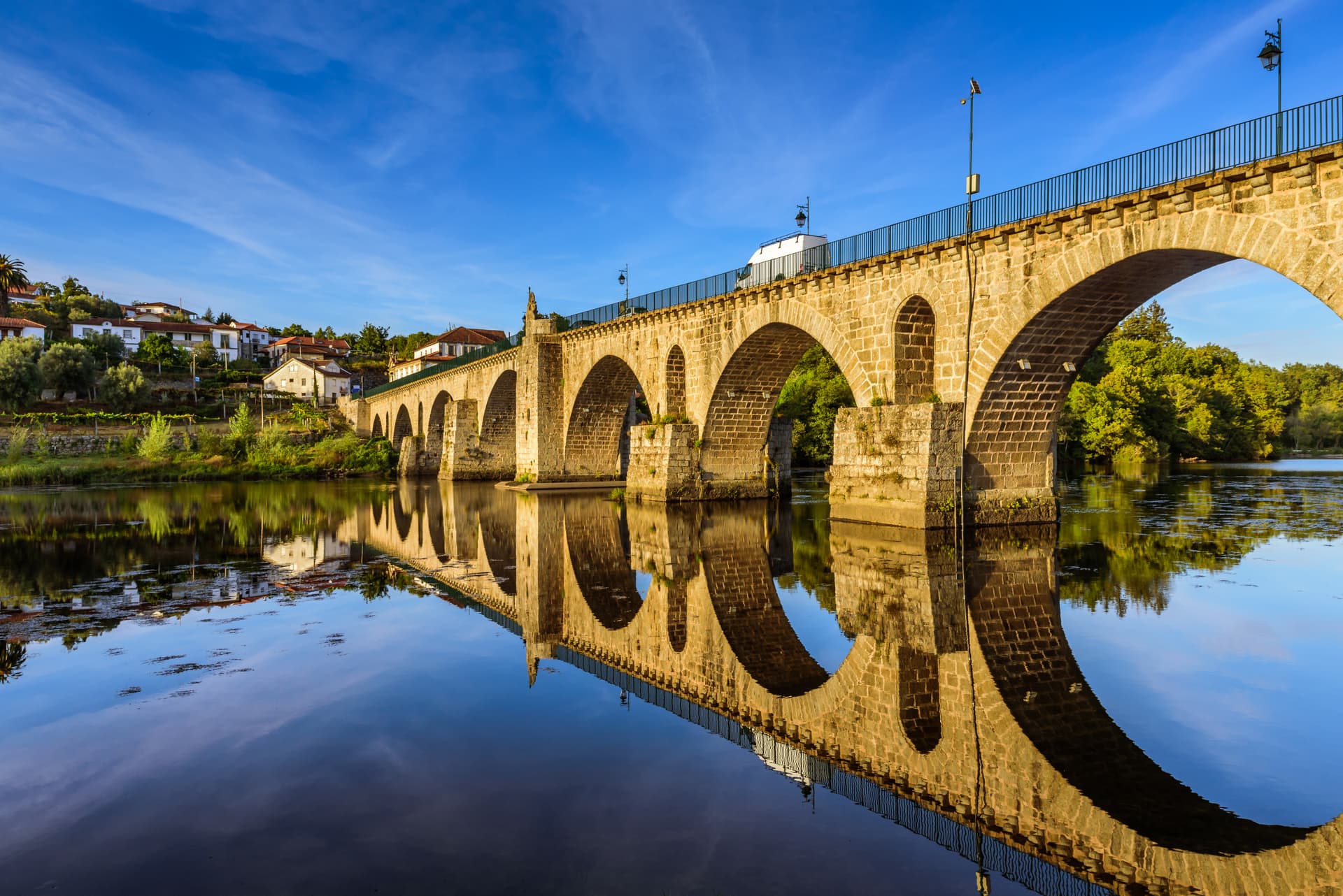 Stone bridge over river with perfect reflection under blue sky near Ponte da Barca, Portugal.