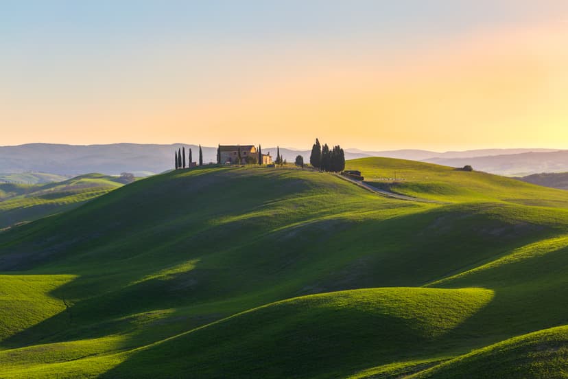 Tuscan farmhouse on rolling green hills at sunset