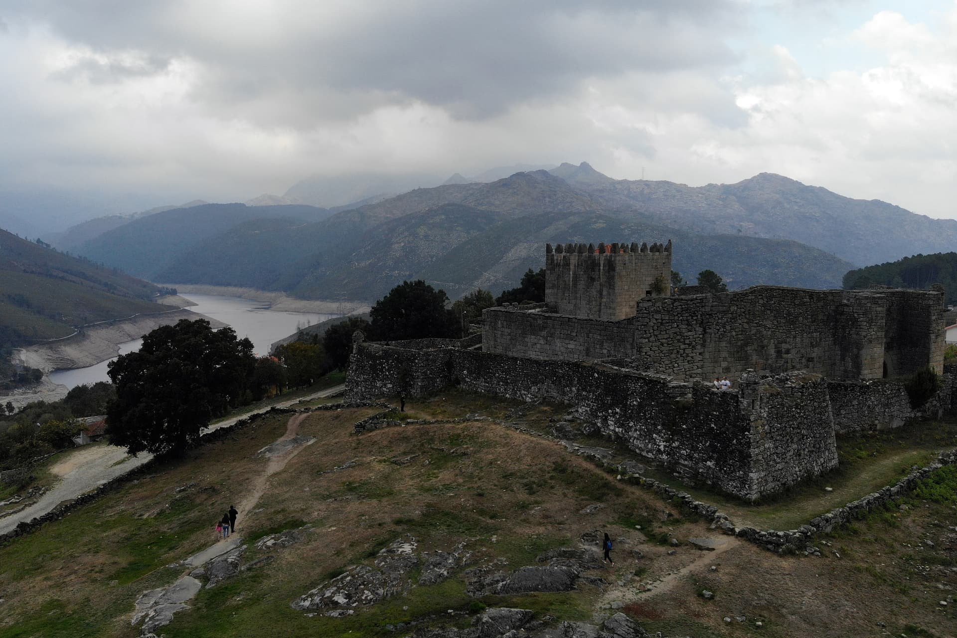 Castelo de Lindoso stone fortress overlooking a reservoir and rugged mountains under a cloudy sky.