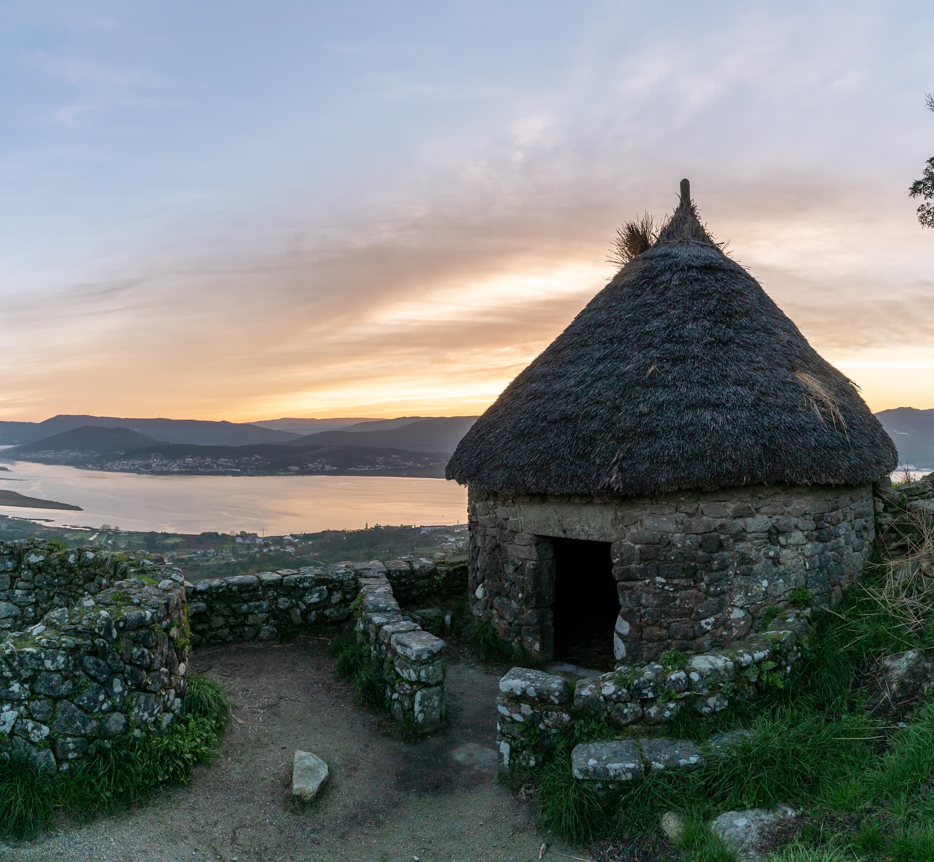 Replica Celtic hut with thatched roof at Castro site overlooking A Guarda, Galicia, at sunset.