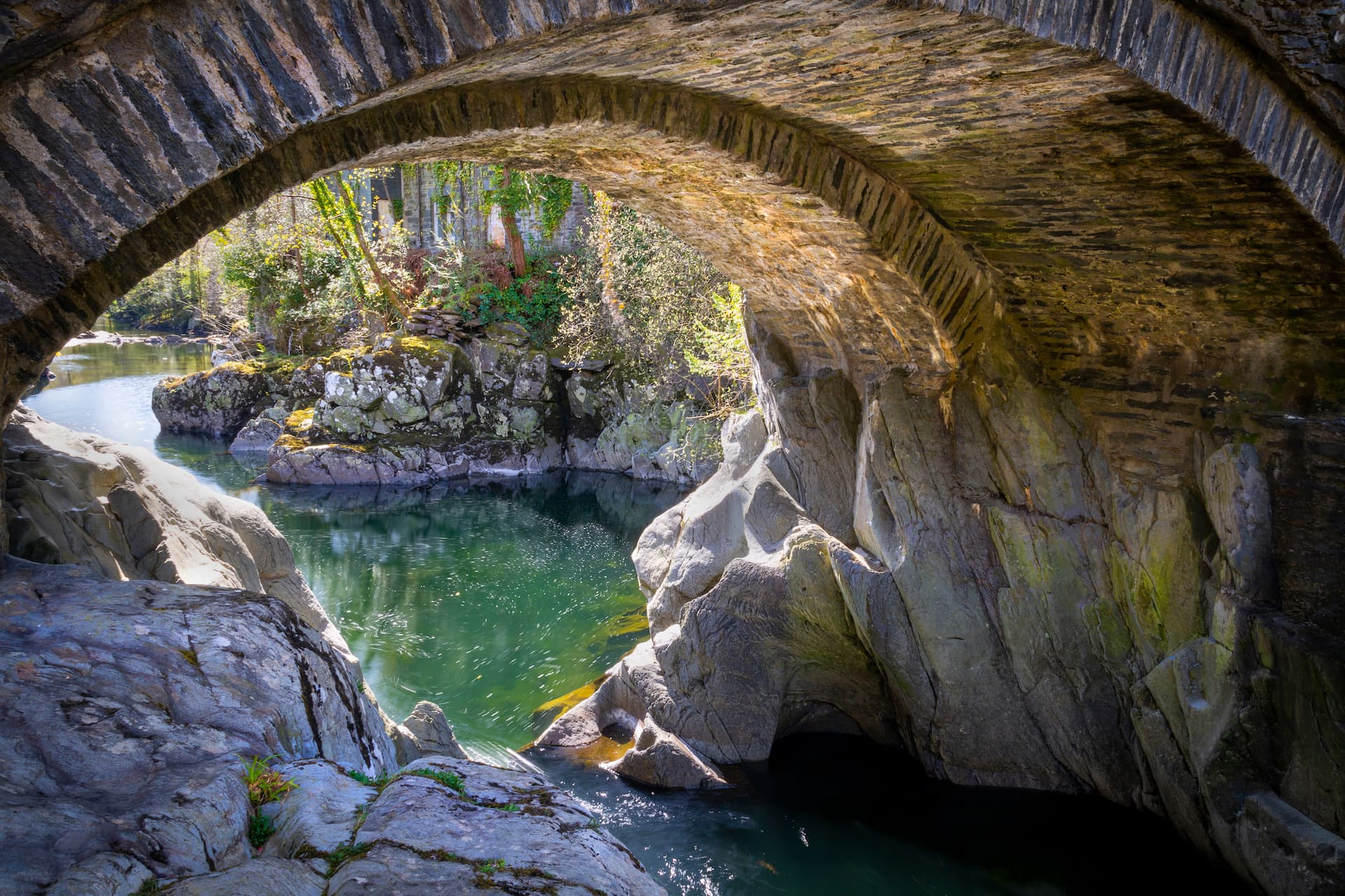Stone arch bridge over a river gorge with green water and rocky banks in Betws-y-Coed.
