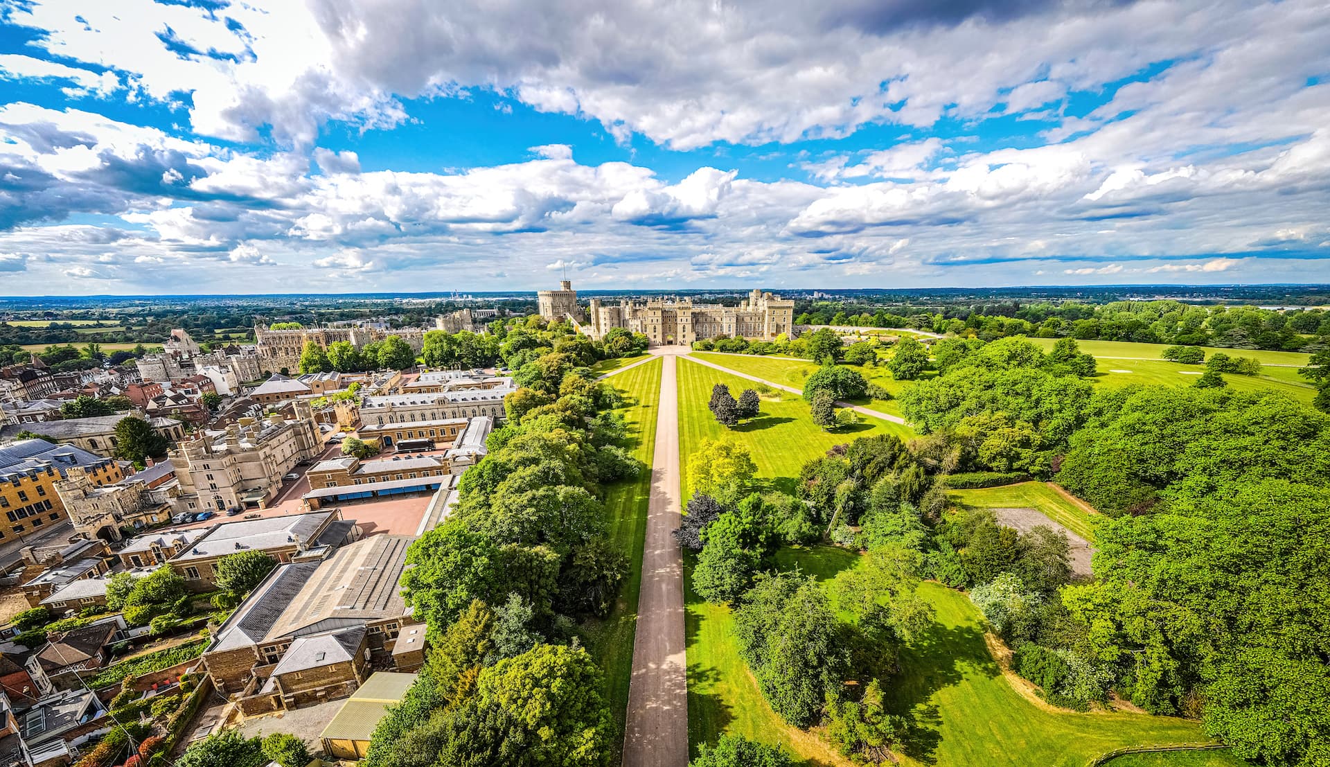 Windsor Castle overlooking town and Long Walk with green parkland under cloudy sky.