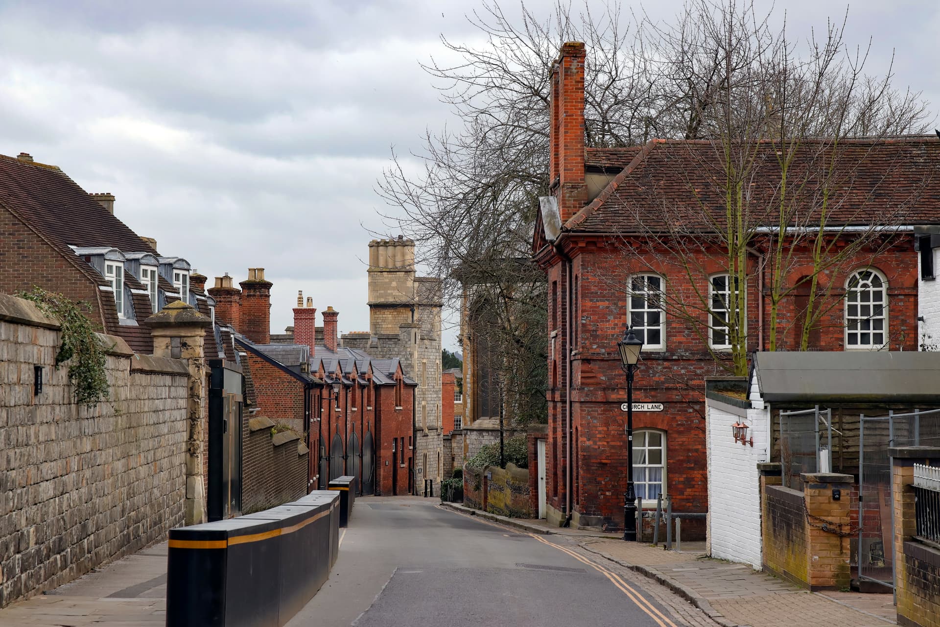 Street scene on Church Lane with red brick buildings and a stone tower under a cloudy sky.