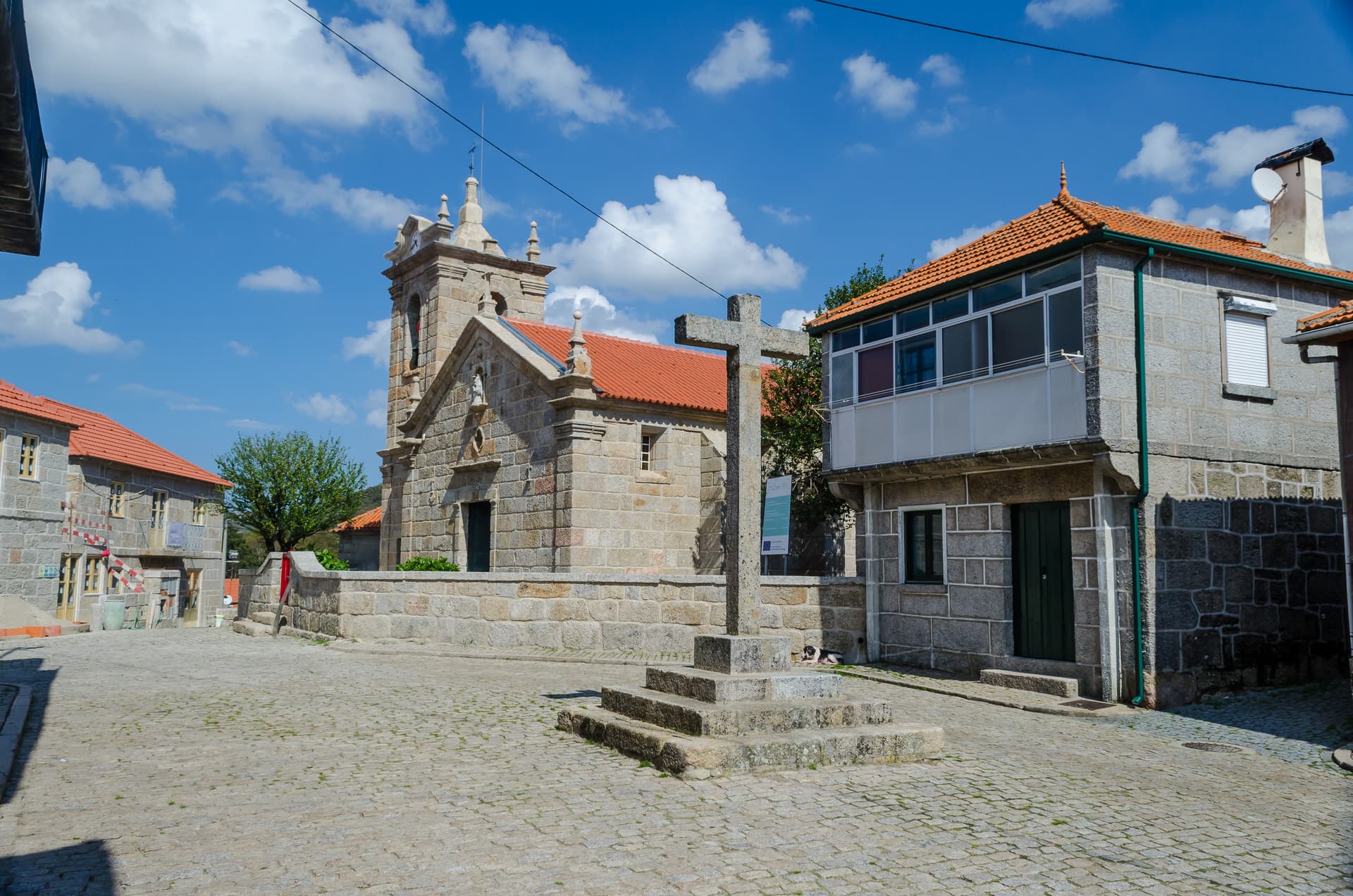 Stone church and calvary cross in the cobbled Plaza del Pueblo de Castro Laboreiro, Melgaço, Portugal.
