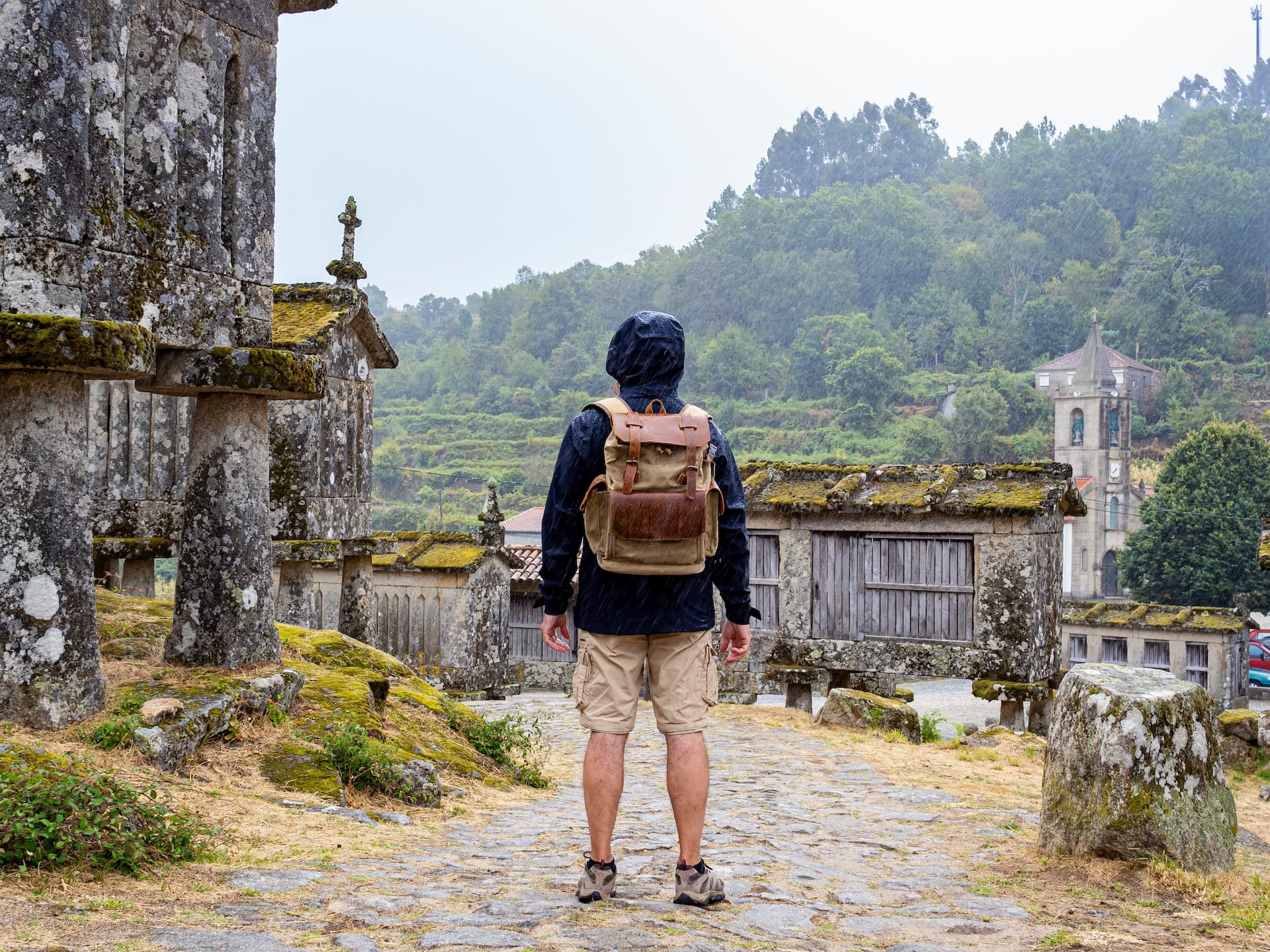 Hiker looking at historic stone granaries in Lindoso, Portugal, as it rains.