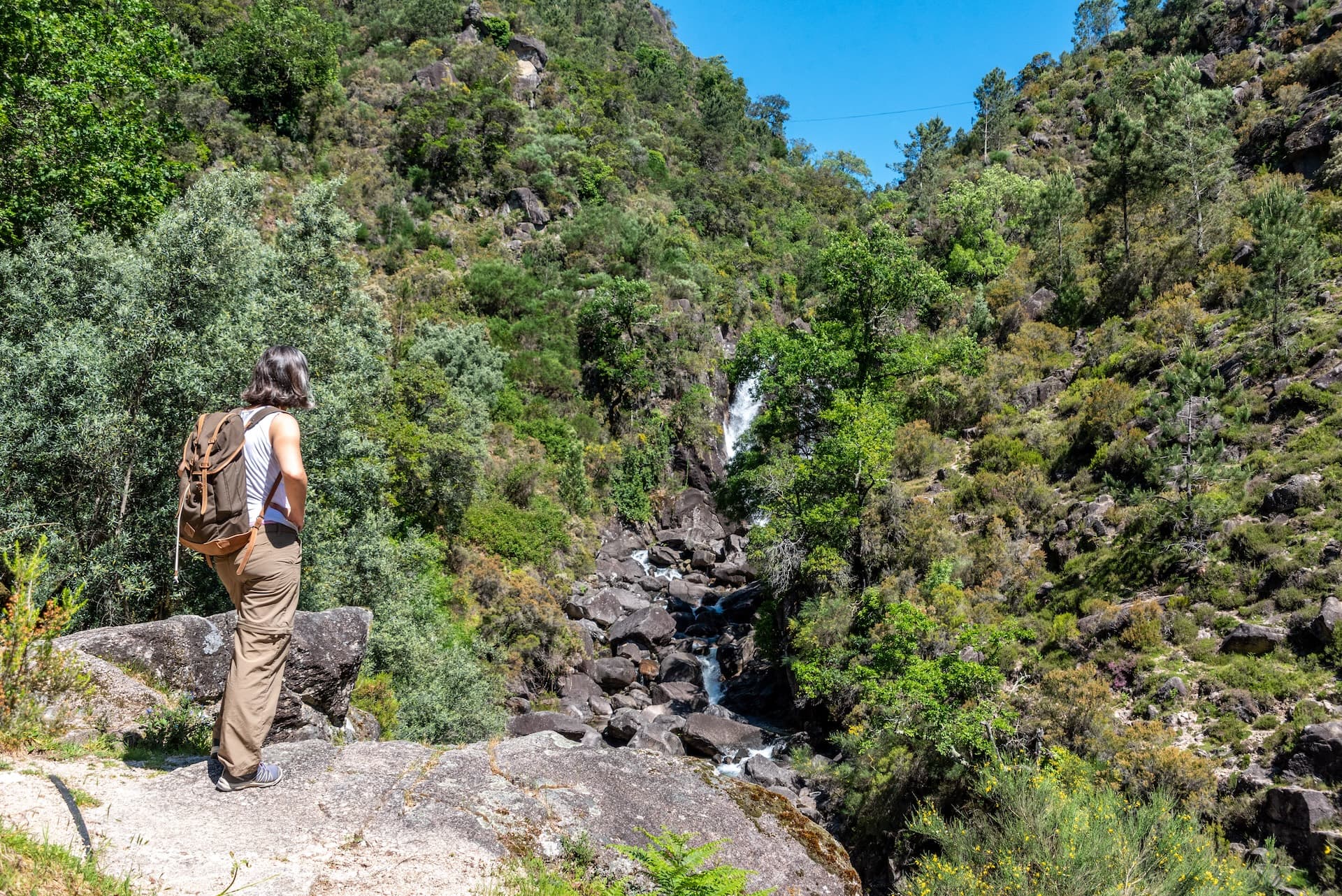 Hiker overlooking Rajada waterfall cascading over rocks in Peneda-Gerês National Park, Portugal.