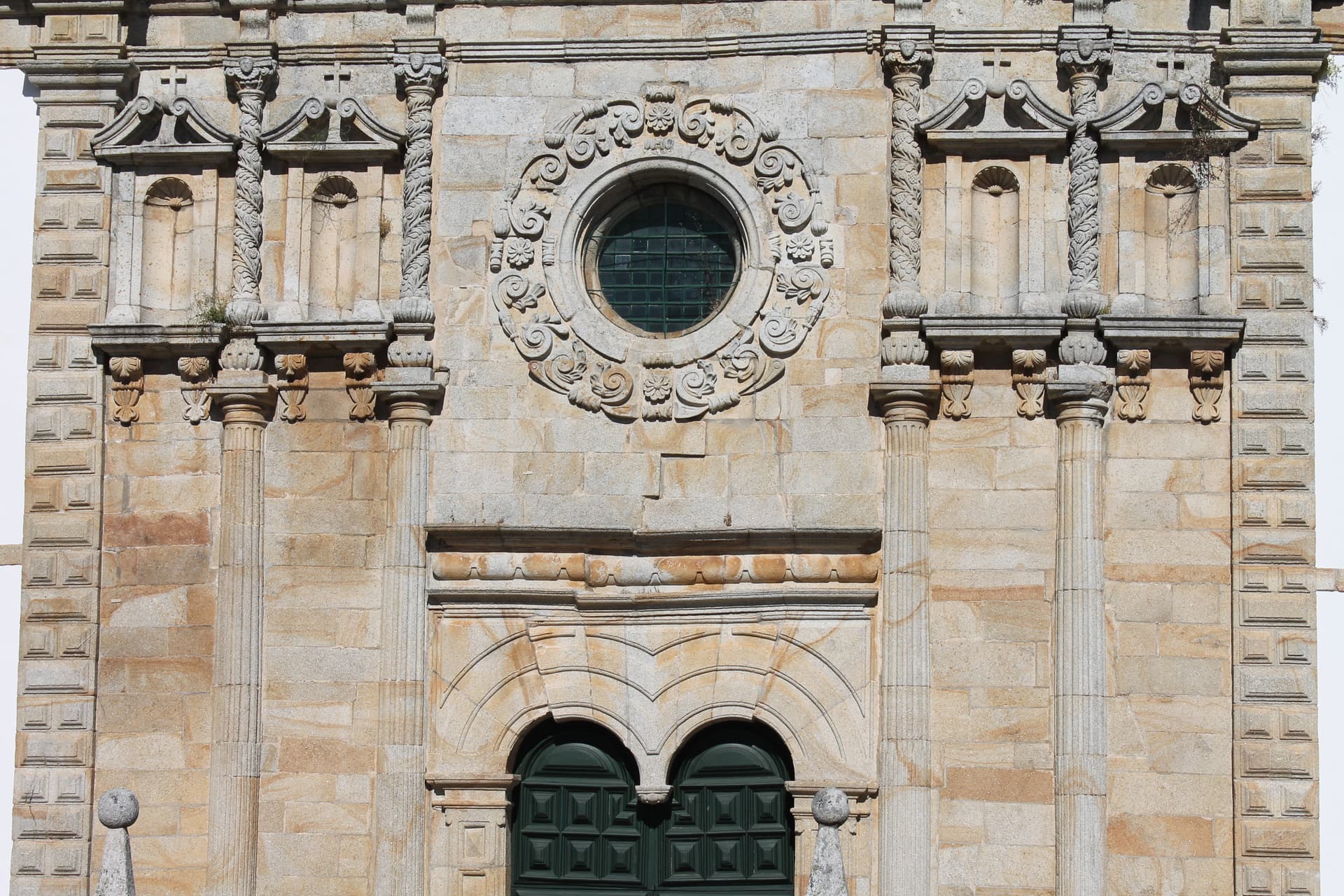 Ornate stone facade of Holly Christ minor basilica with round window and arched doorways in Outeiro, Portugal.