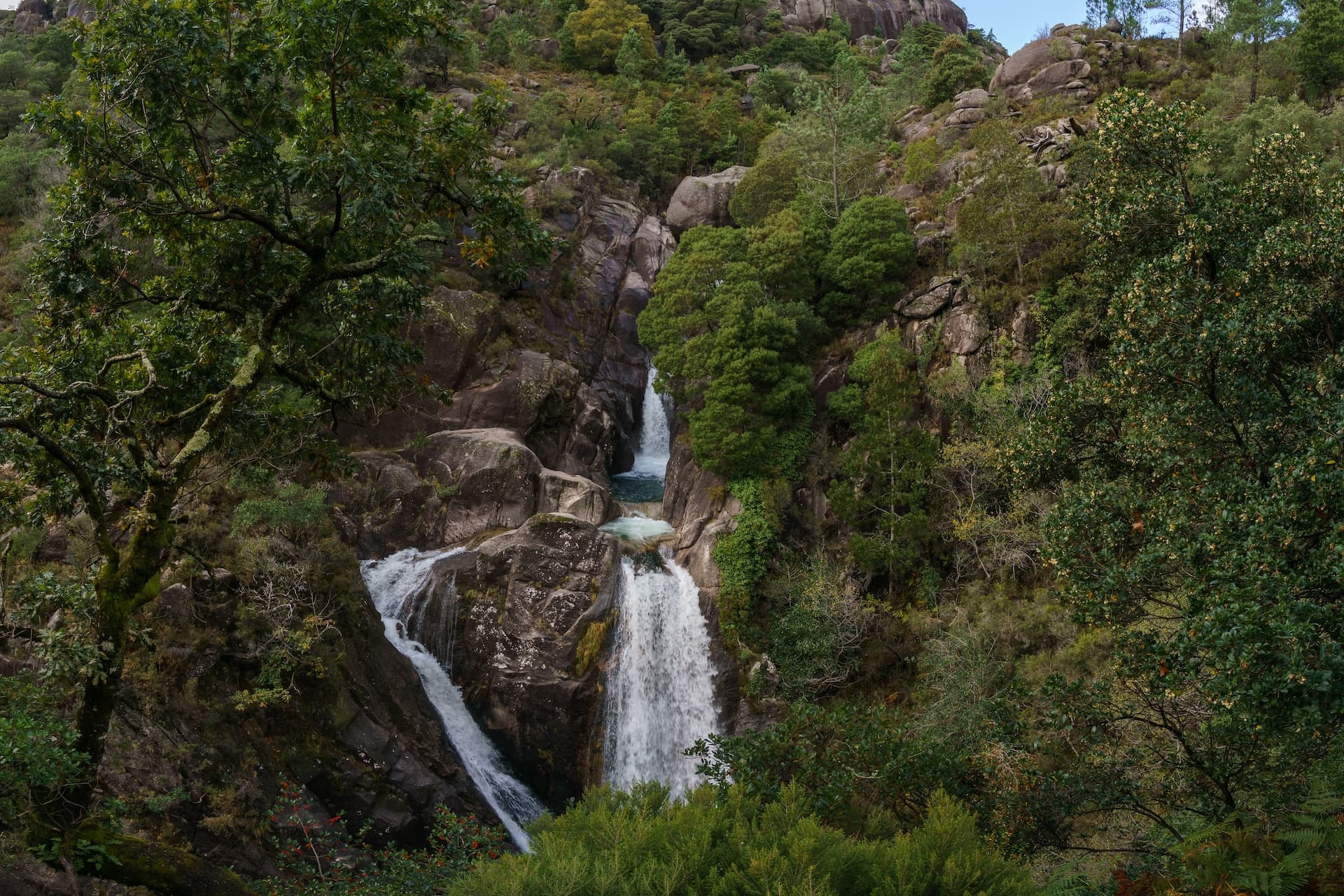 Cascata do Arado waterfall cascading down rocks surrounded by lush green forest in Peneda-Gerês National Park.