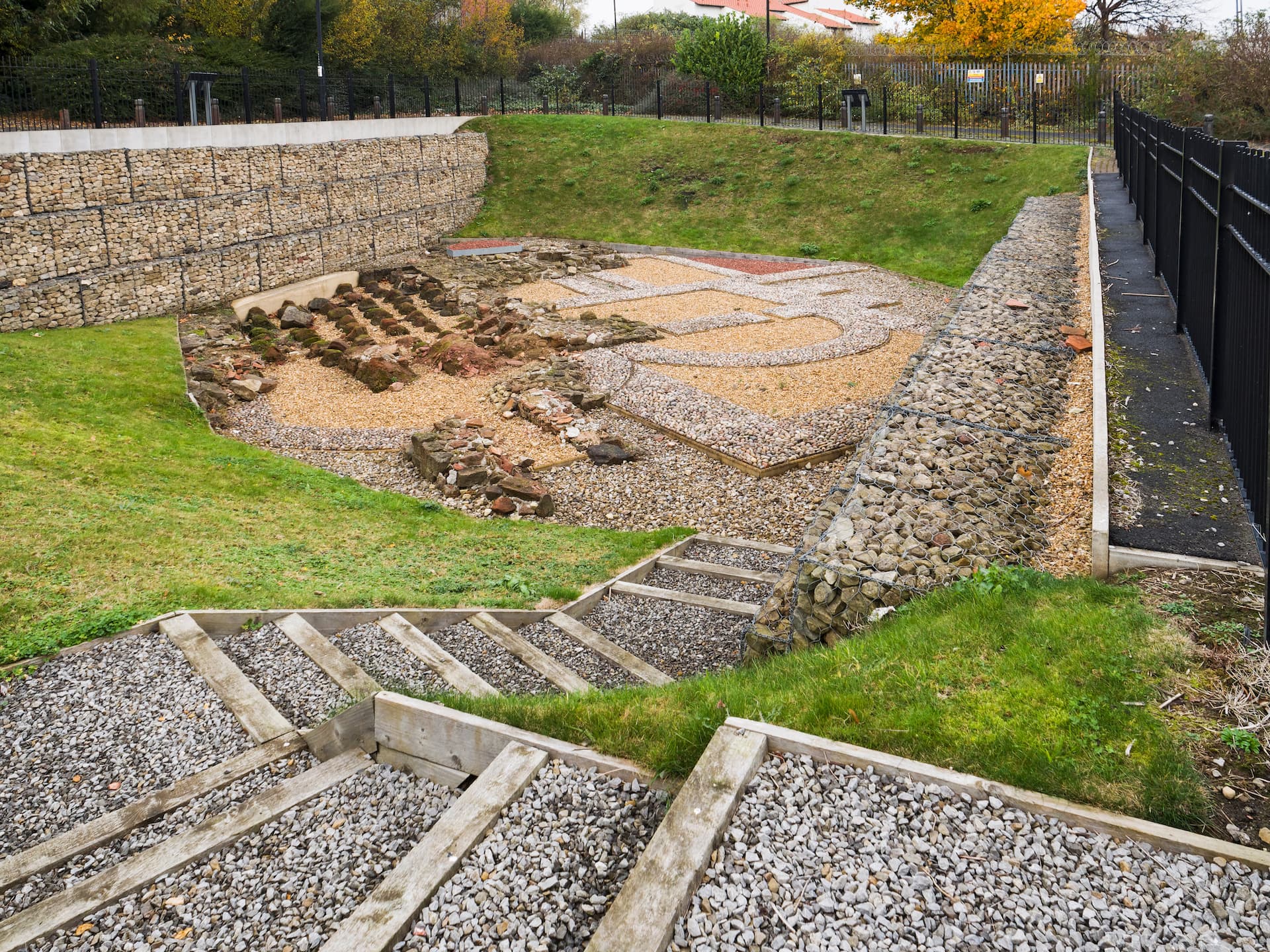 Roman Fort Baths ruins display with gravel paths, retaining walls, and wooden steps in Wallsend.
