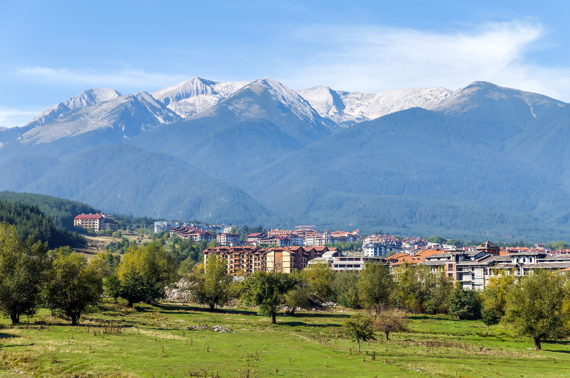 Alpine village nestled below snow-capped mountains with green foreground meadow in Bansko.