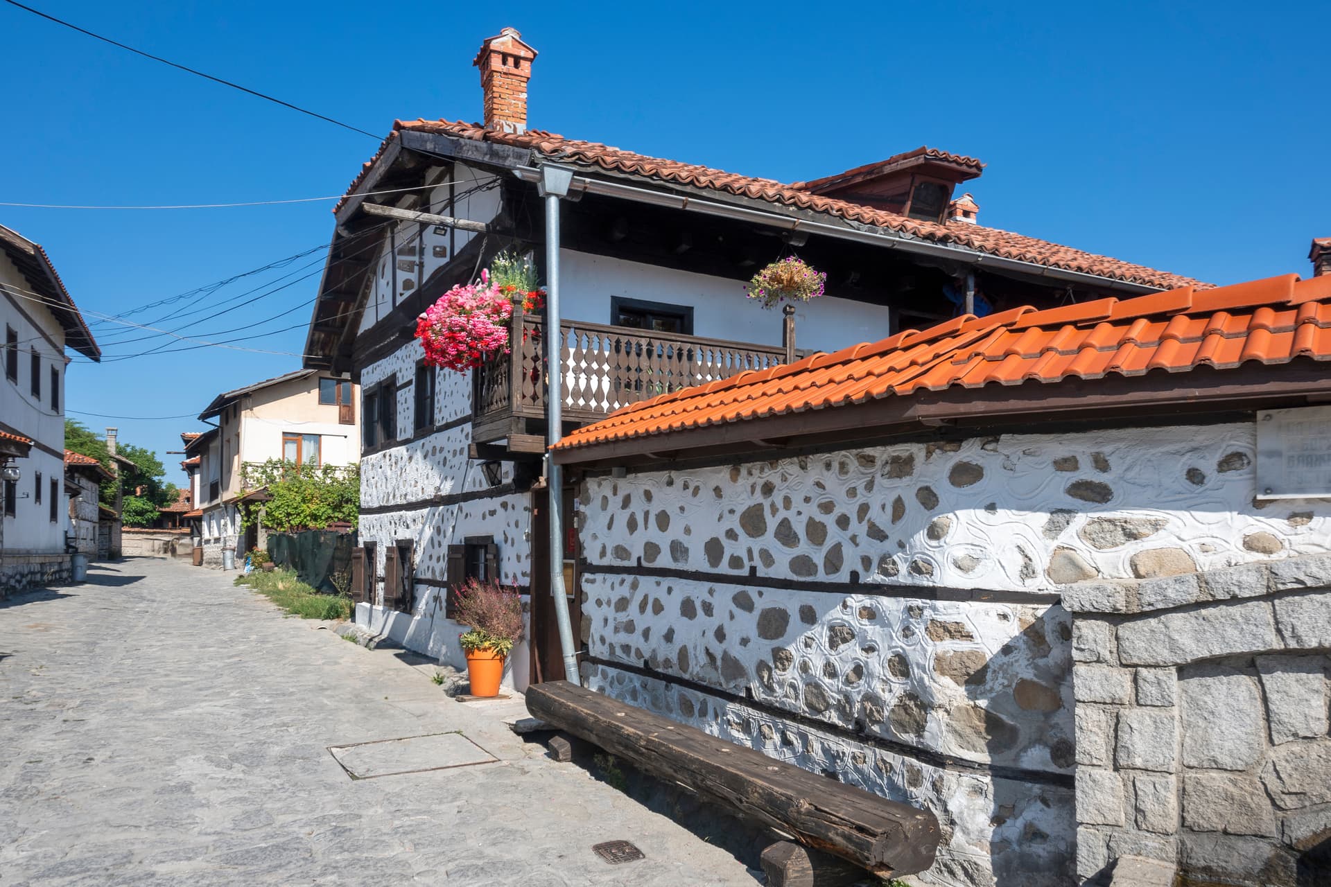 Stone street in Bansko with traditional white and stone house featuring a wooden balcony.