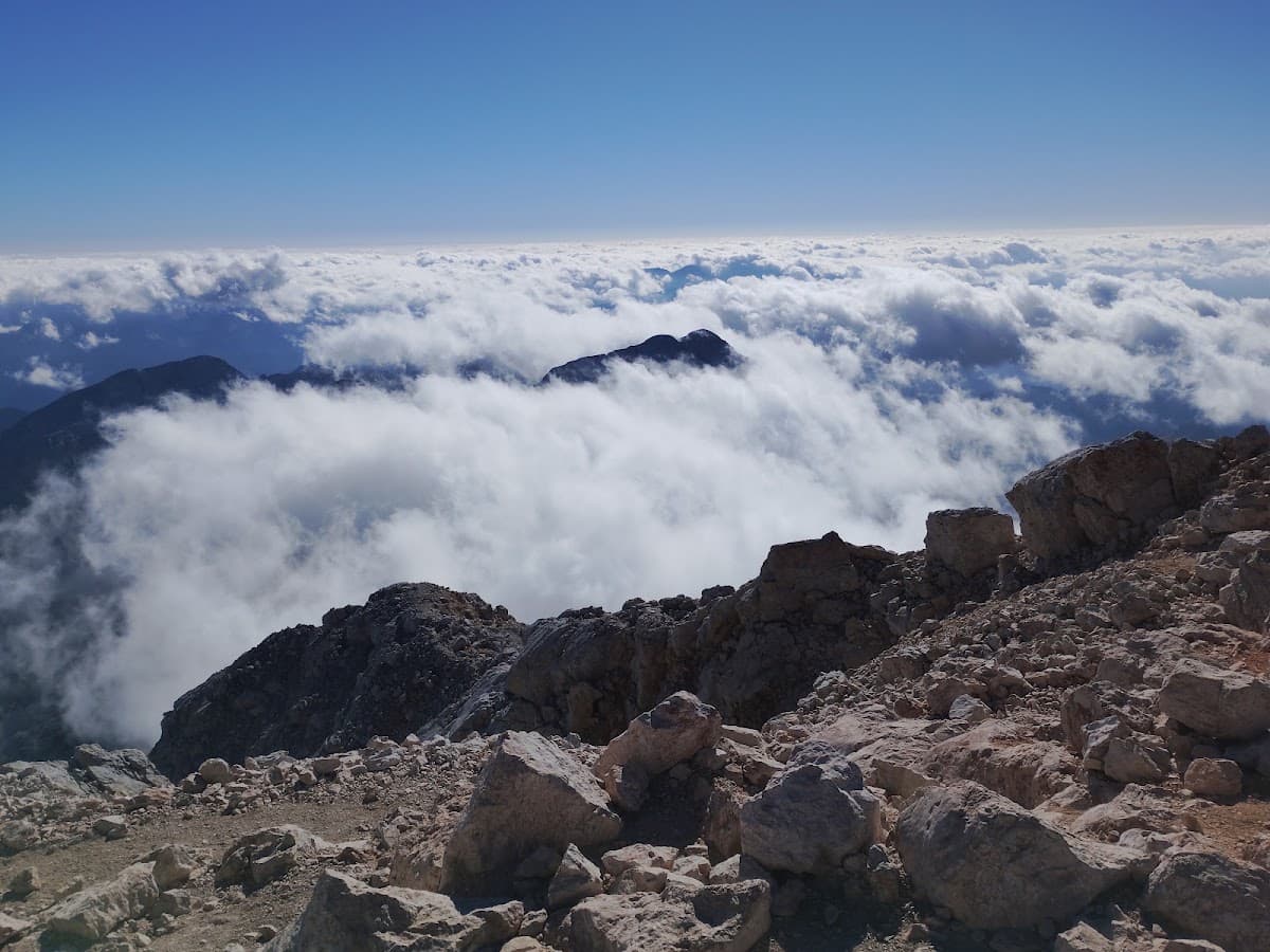 Rocky mountain summit above a sea of clouds under a clear blue sky