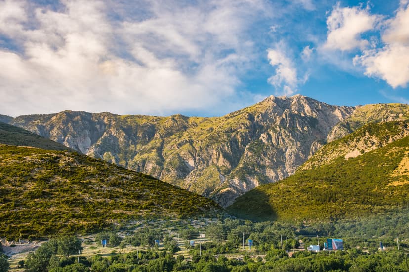 Rugged mountain peaks with green hills and blue sky with clouds