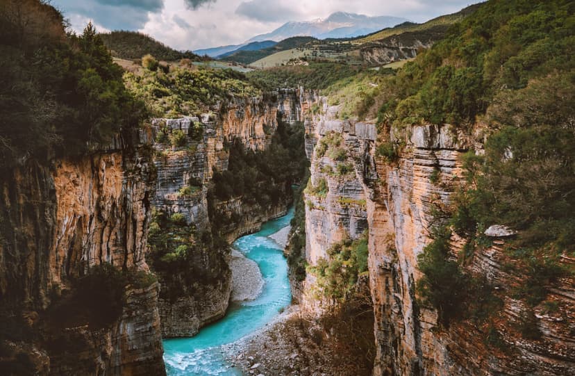 Turquoise river flowing through a deep rocky canyon with steep cliffs and mountain background