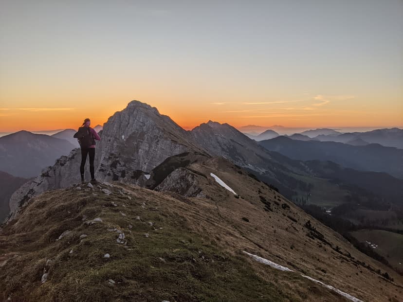 Hiker standing on mountain ridge overlooking peaks at sunset