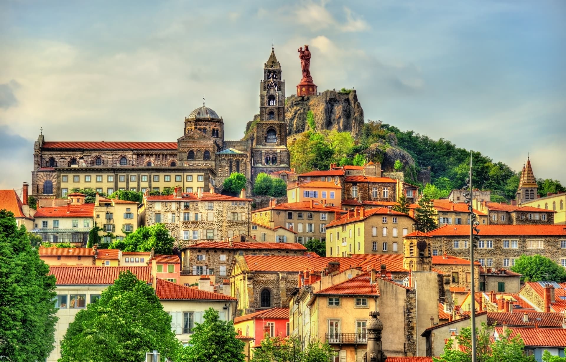 View of Le Puy-en-Velay, France, with colorful rooftops, cathedral, and statue atop a rocky outcrop.