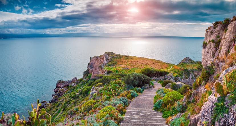 Stone staircase descending coastal cliff with green vegetation overlooking the sea at sunset