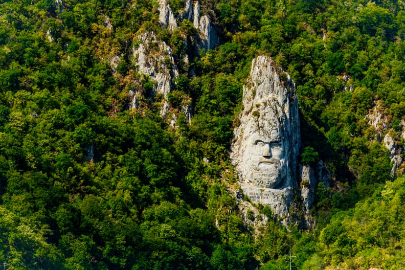 Giant stone face carved into a rocky cliffside surrounded by green forest