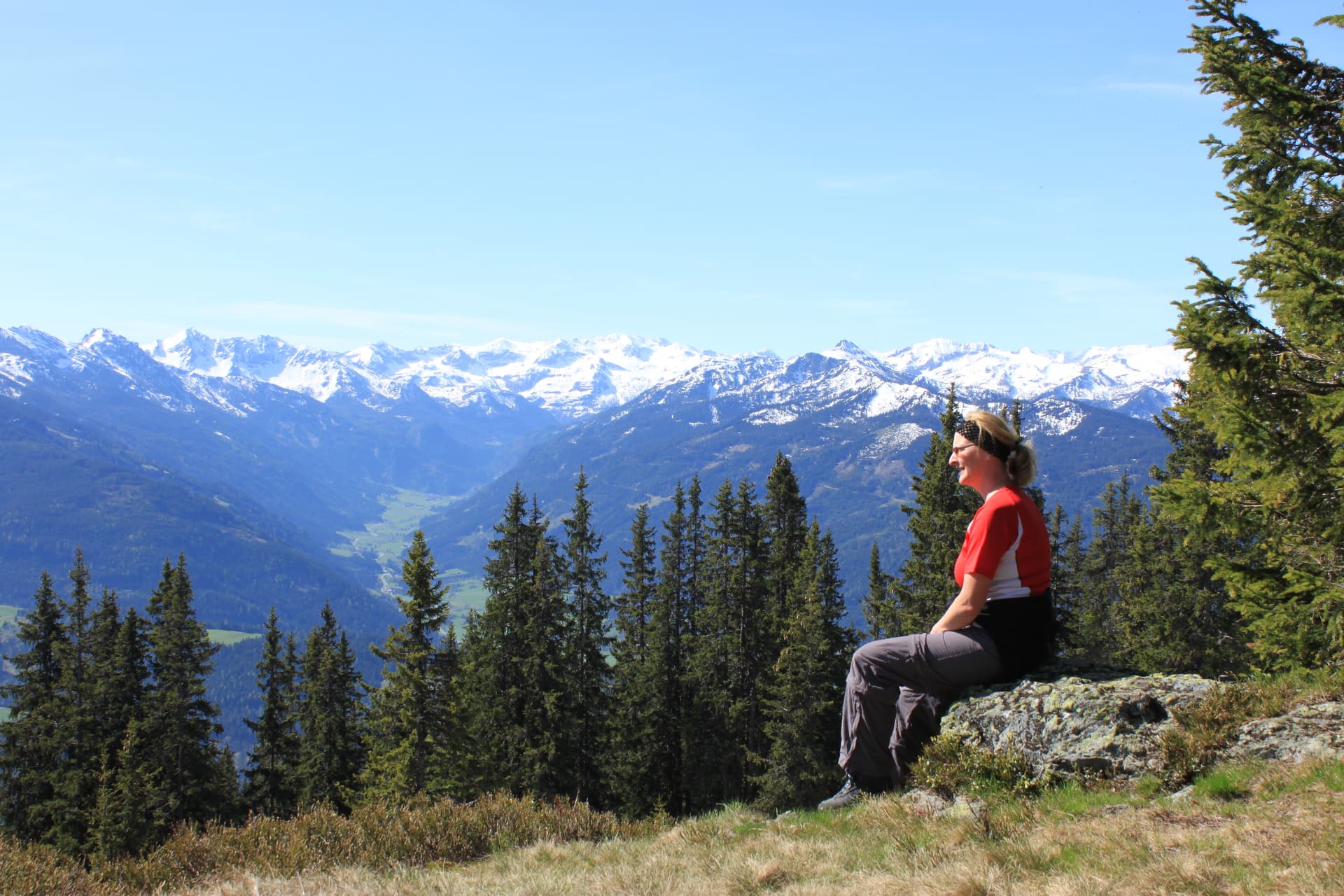 Hiker resting on rock overlooking snowy alpine peaks and valley in Radstadt, Austria.