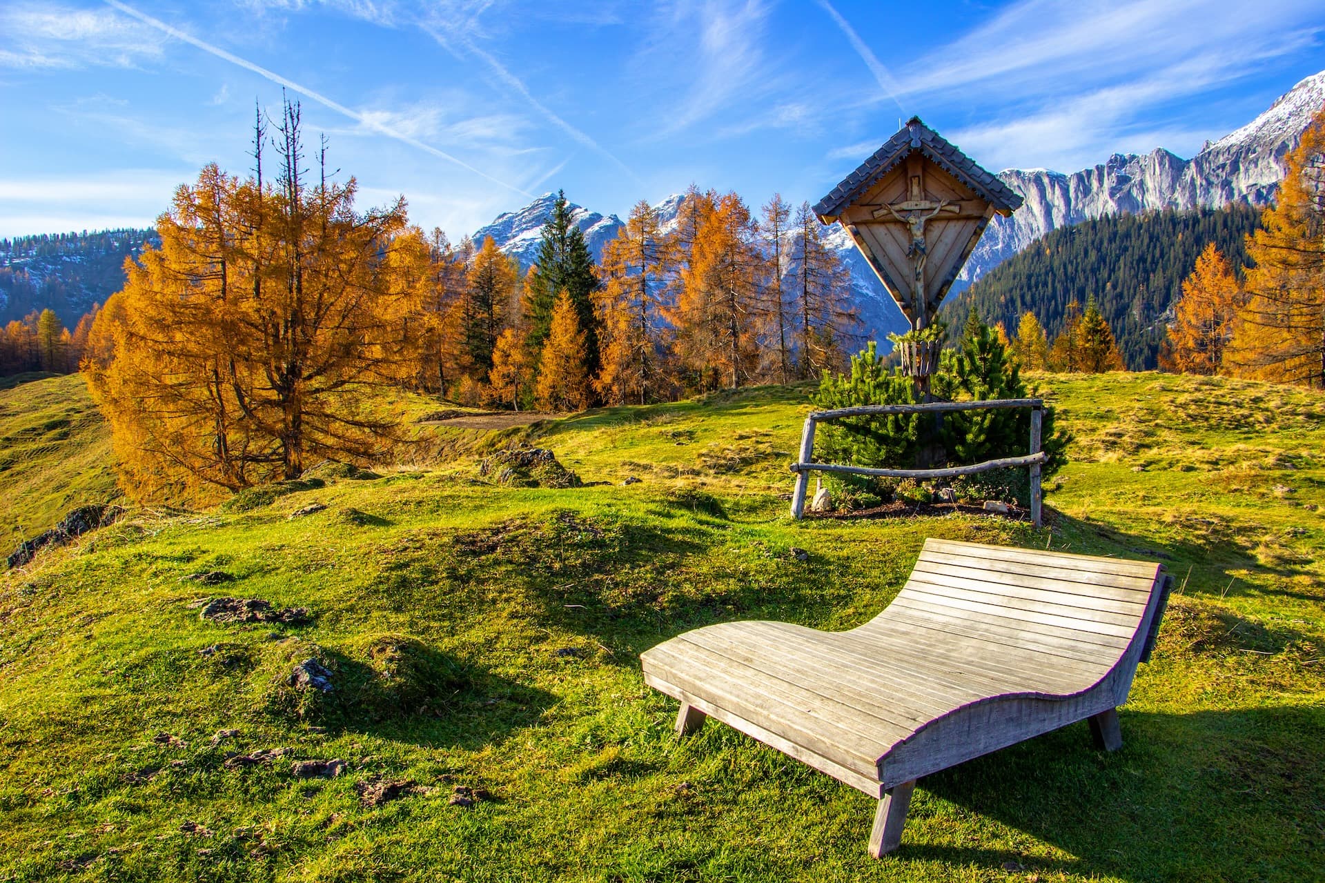 Wooden lounge chair and wayside shrine on grassy alpine meadow near St. Martin am Tennengebirge.