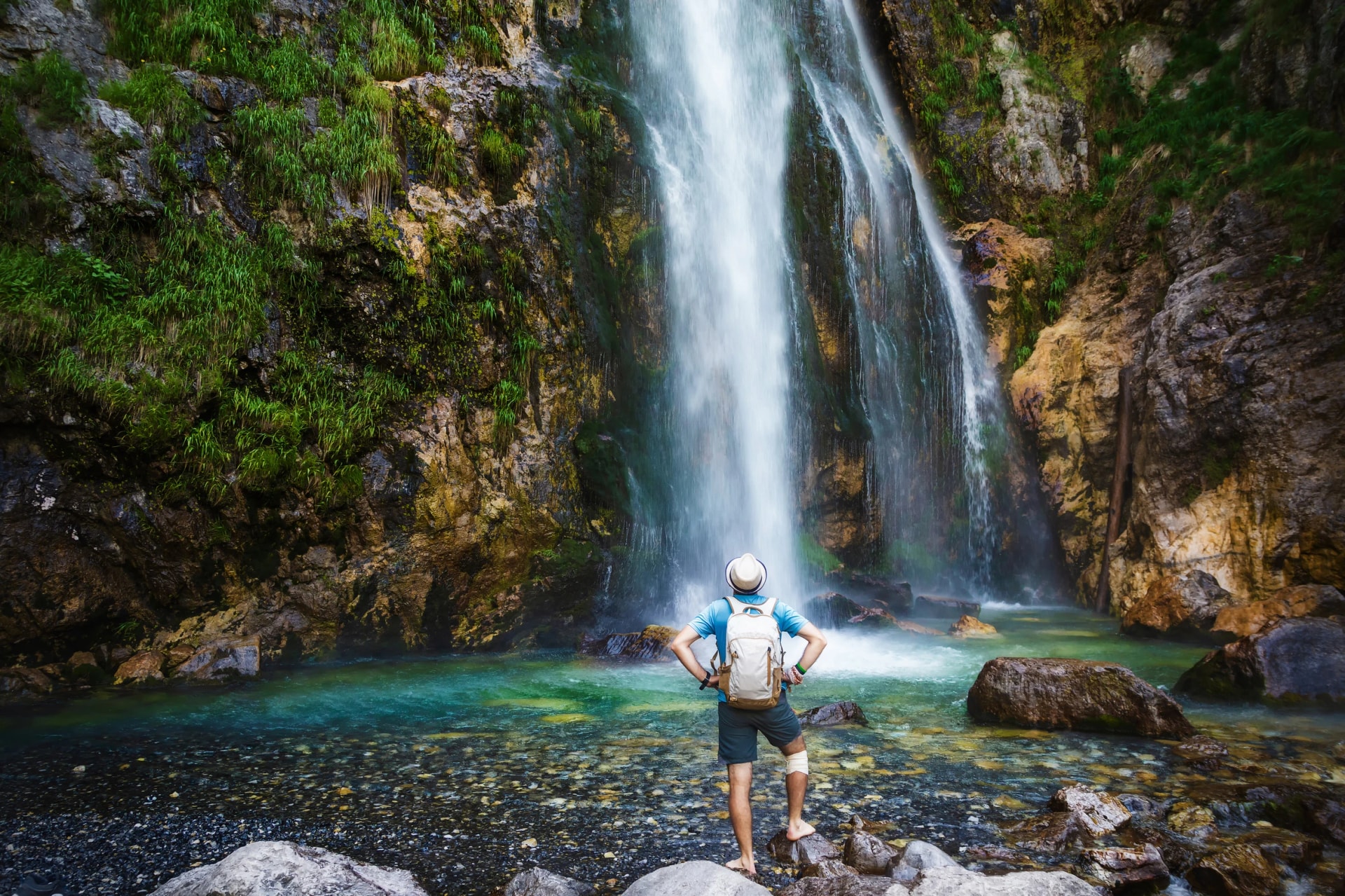 A man in a hat stays under the streams of the waterfall. Grunas Waterfall is a picturesque site inside the National Park of Thethi, Albania
