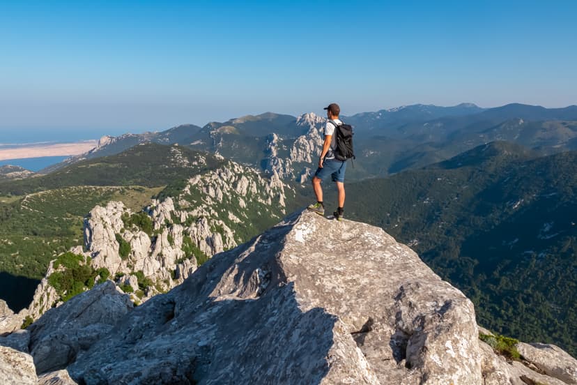 Hiker standing on rocky mountain summit overlooking distant mountain ranges and sea
