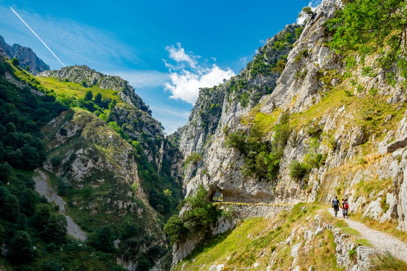 Hikers walking on a mountain trail through a steep rocky gorge under a blue sky