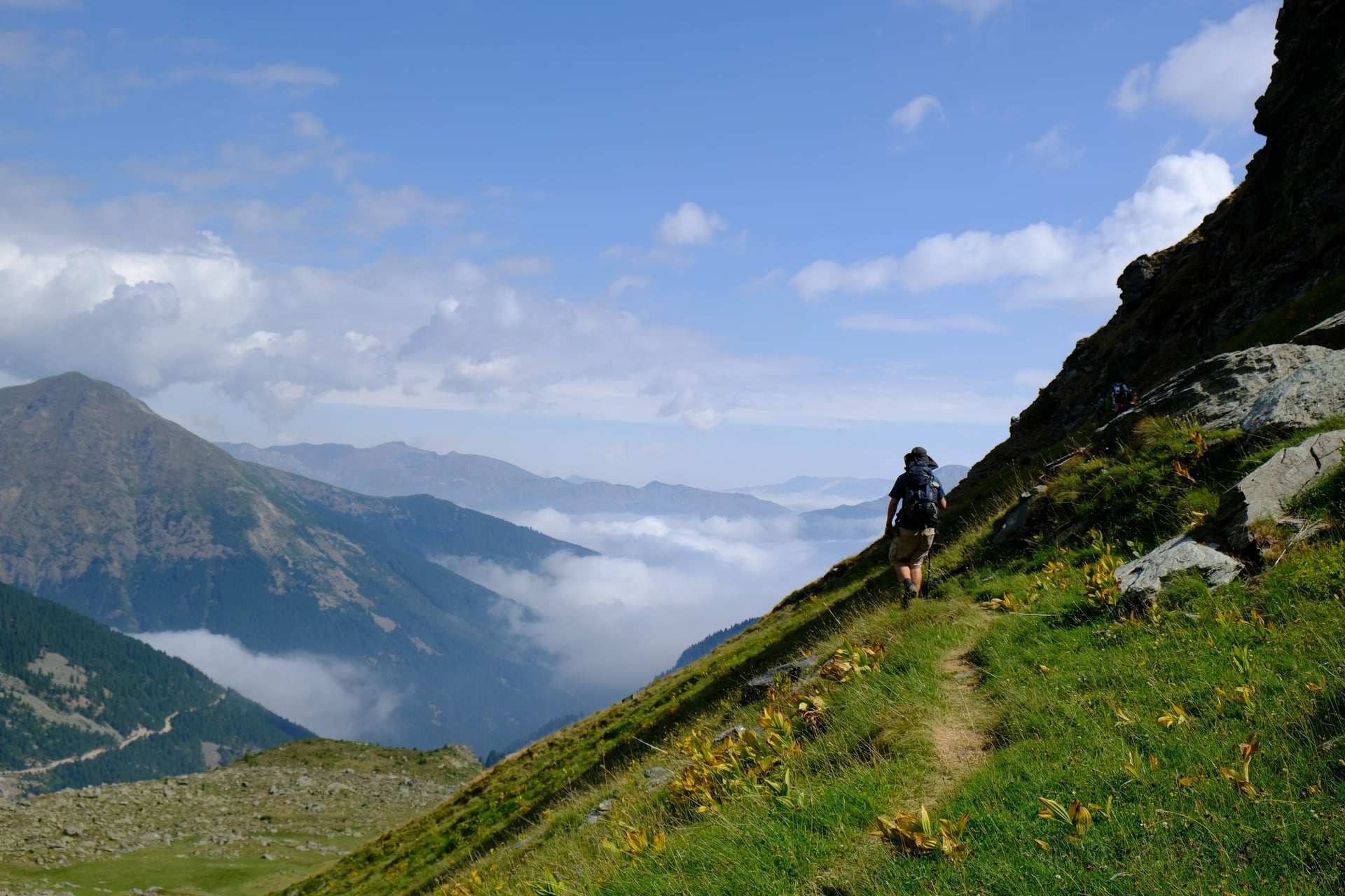 Hiker on mountain trail above clouds with peaks in the background