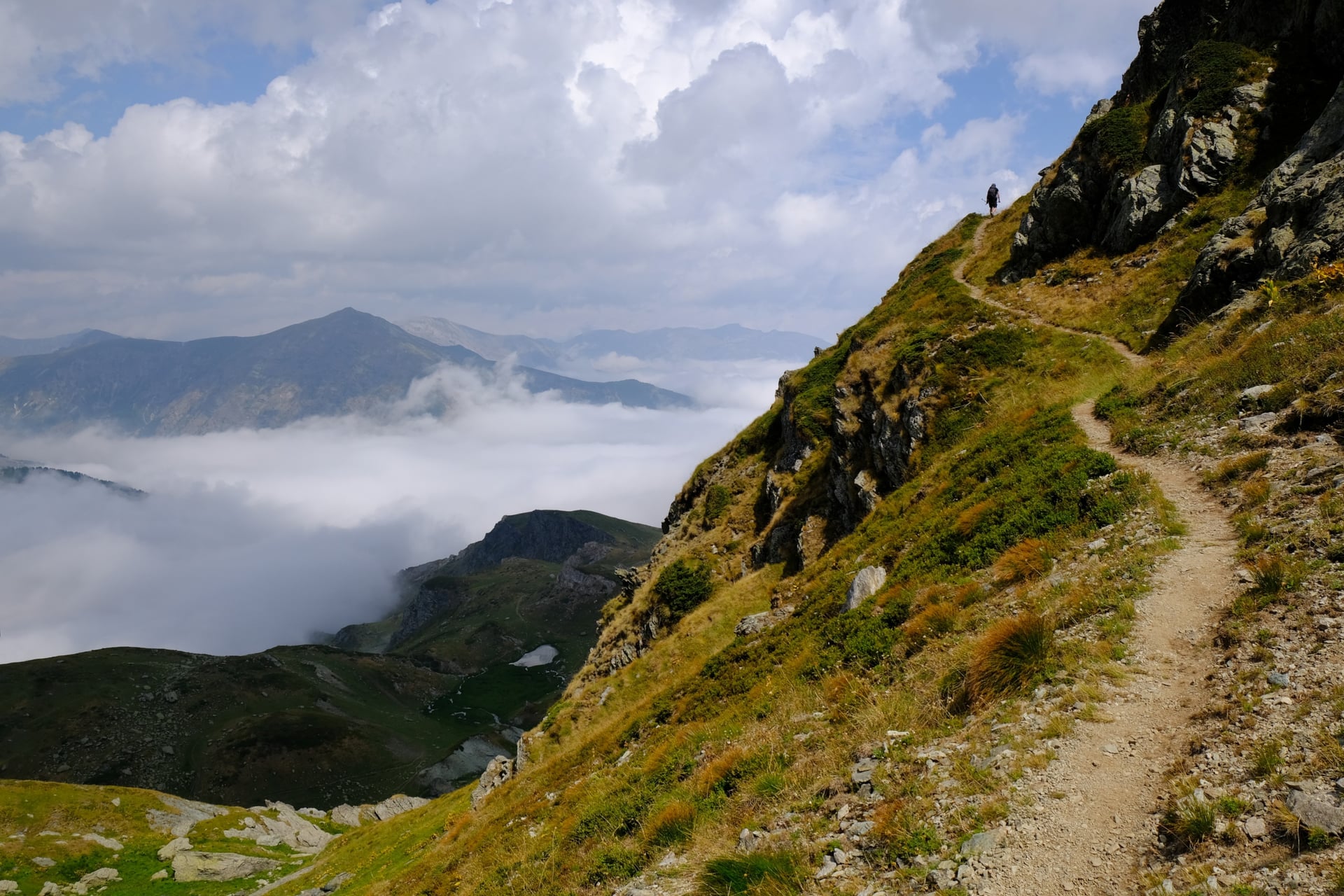 Hiker on mountain trail above clouds with distant peaks