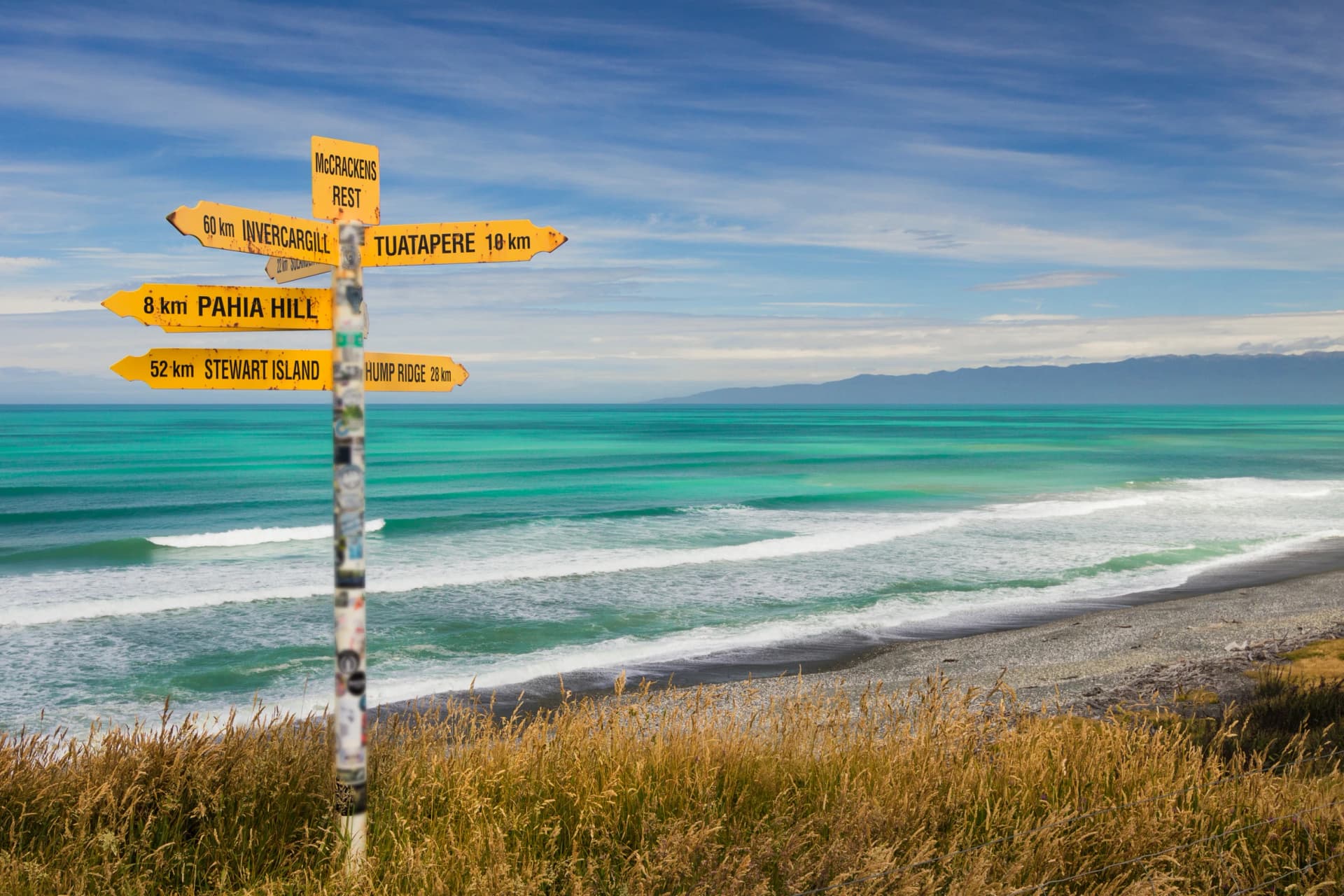 Distance and direction signpost on a beautiful, sunny beach. McCracken's Rest, Southland, New Zealand.