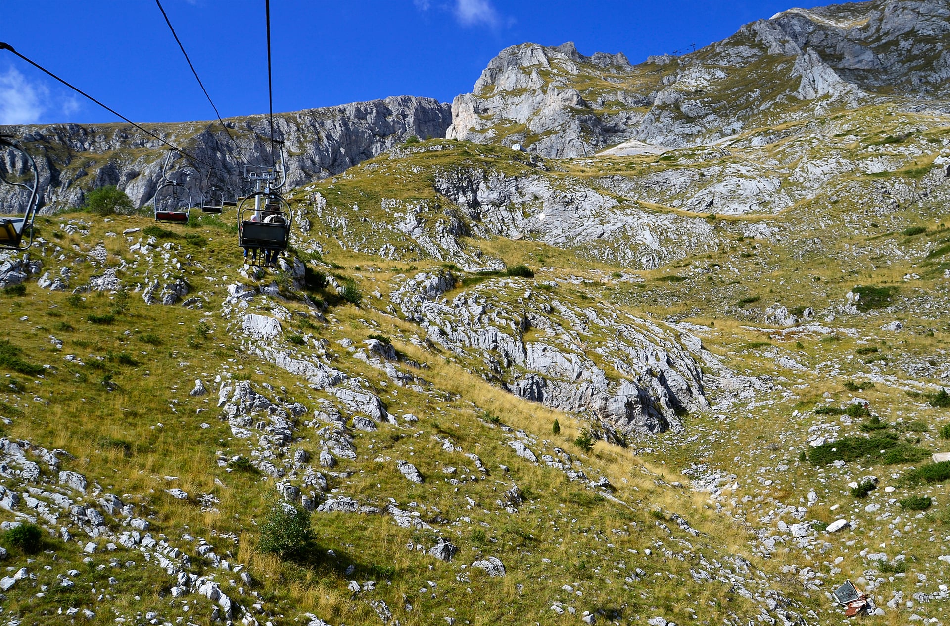 Sessellift, der einen felsigen alpinen Berghang mit spärlicher Vegetation hinauffährt