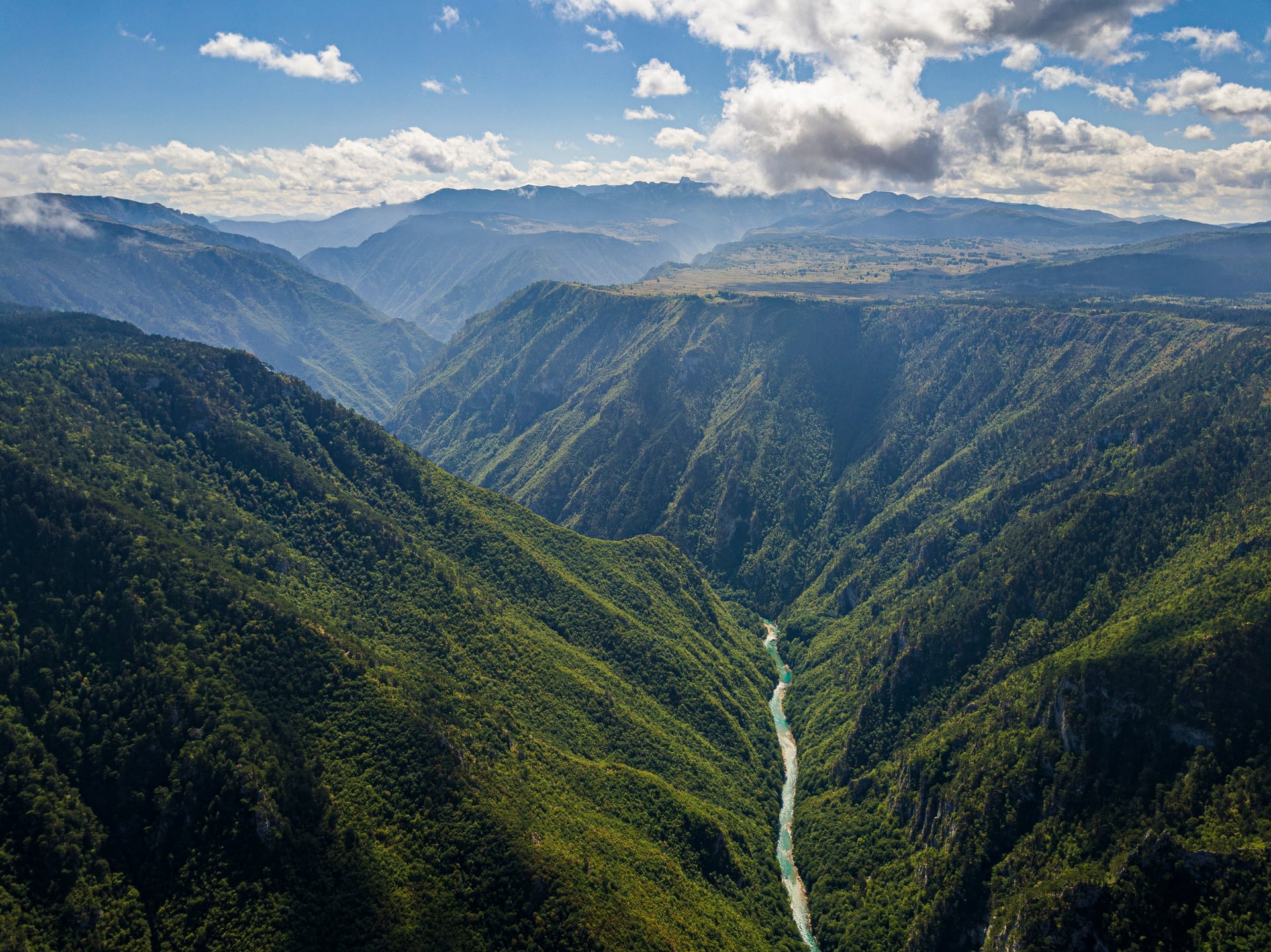 Tiefgrüne Bergschlucht mit einem gewundenen türkisfarbenen Fluss darunter unter einem teilweise bewölkten Himmel