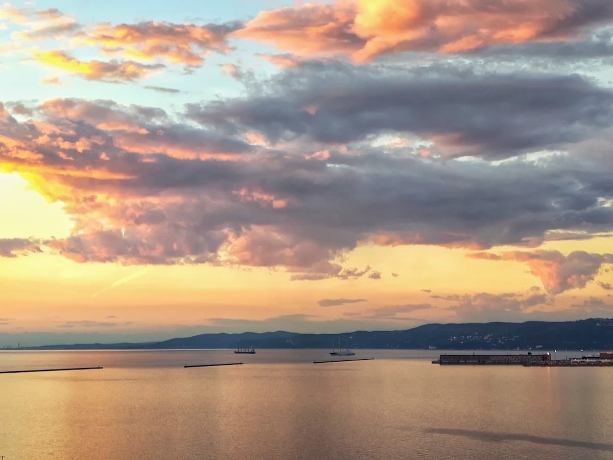 Sunset over calm sea water with distant ships and coastline