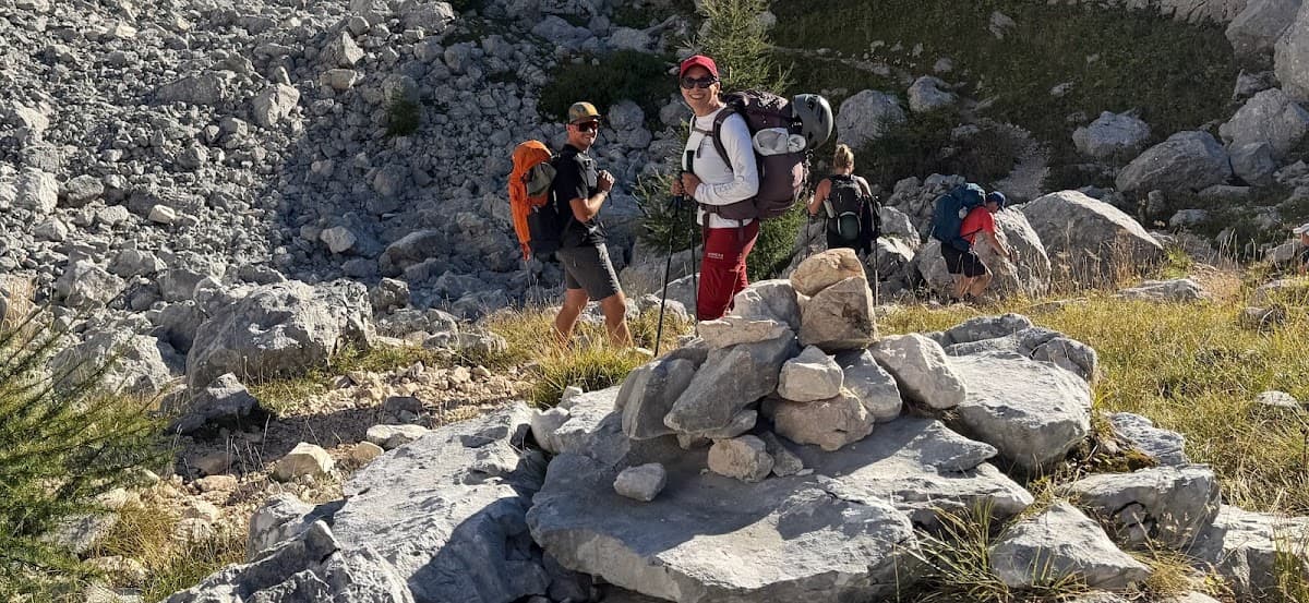 Hikers with backpacks walking on rocky mountain trail with stone cairn