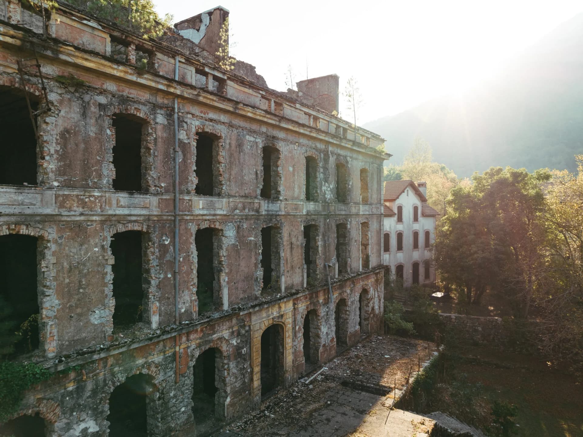 Ruined historic hotel exterior with overgrown vegetation in Vizzavona, Corsica, with bright sunlight.