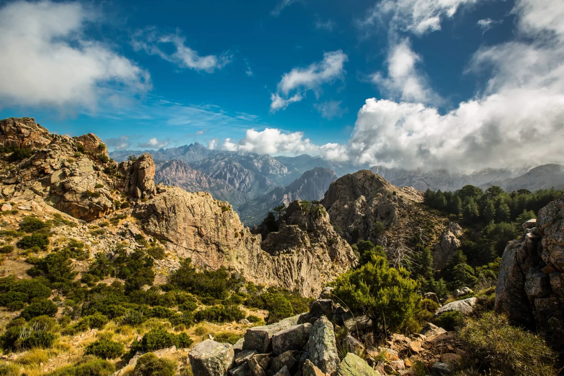 Rocky mountain hiking trail in Corsica under a bright blue sky with white clouds.