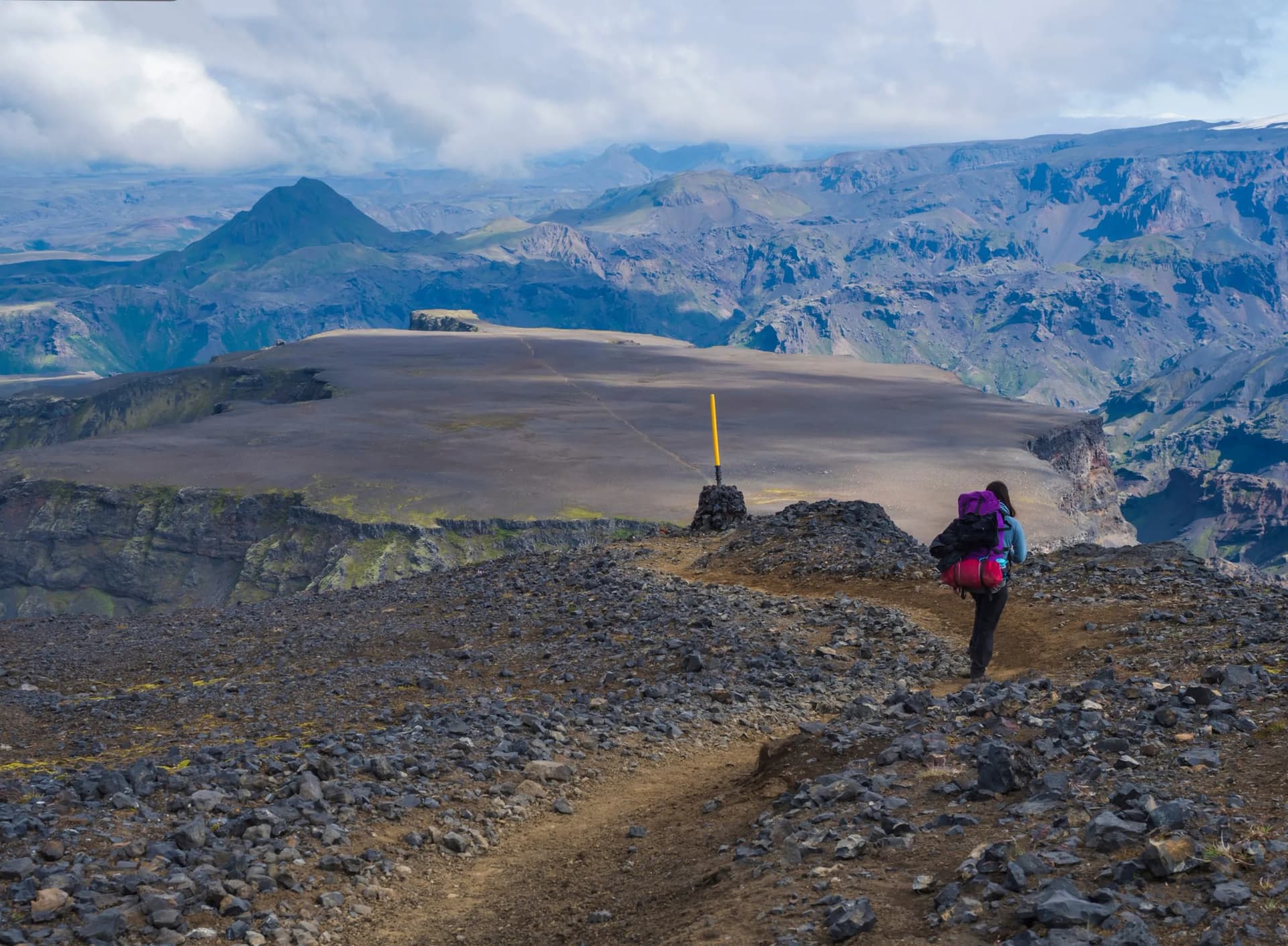 Young woman hiker with backpack at Fimmvorduhals hiking trail. Landscape of Godland with rugged green moss covered rocks and hills, valley of thorsmork, Iceland, Summer blue sky white clouds