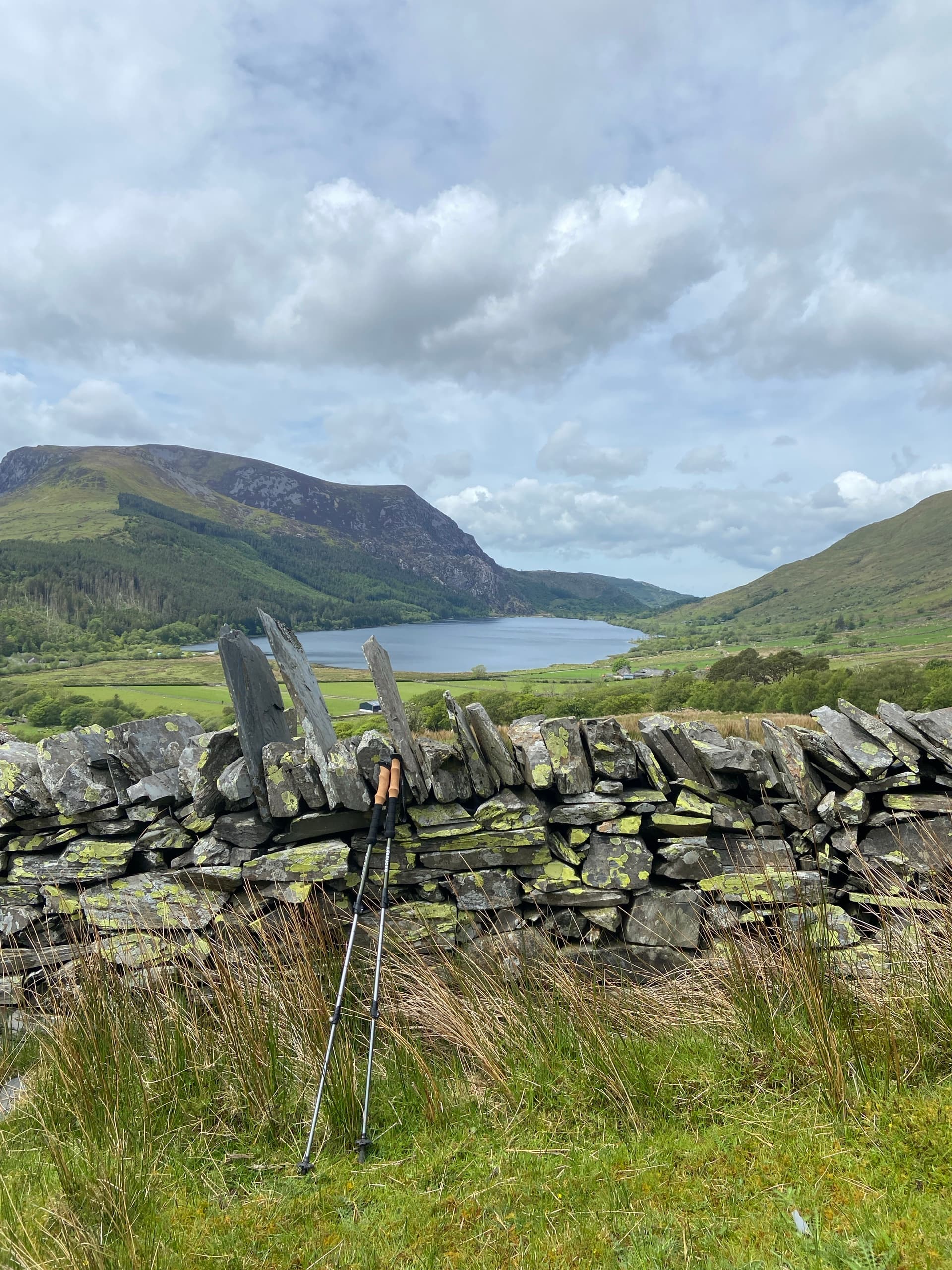Dry stone wall with trekking poles overlooking valley lake and mountains