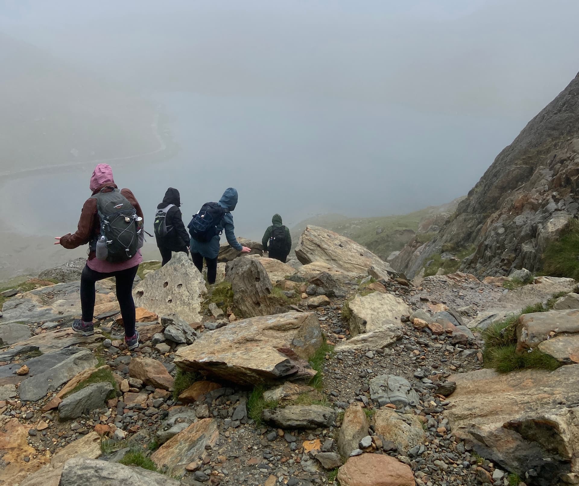 Hikers climbing rocky mountain trail in thick mist