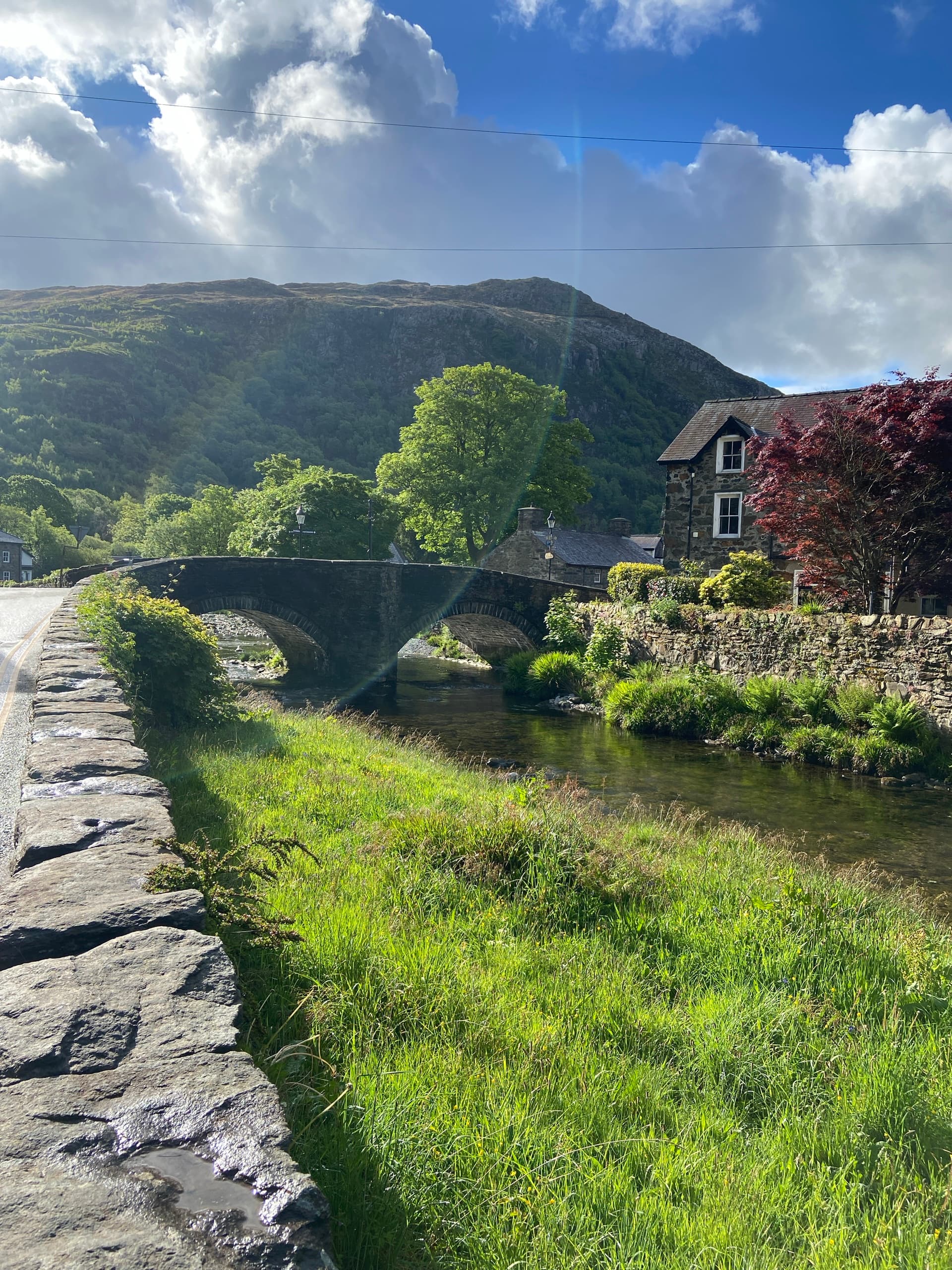 Stone bridge over a river with grassy banks, stone wall, and mountain backdrop
