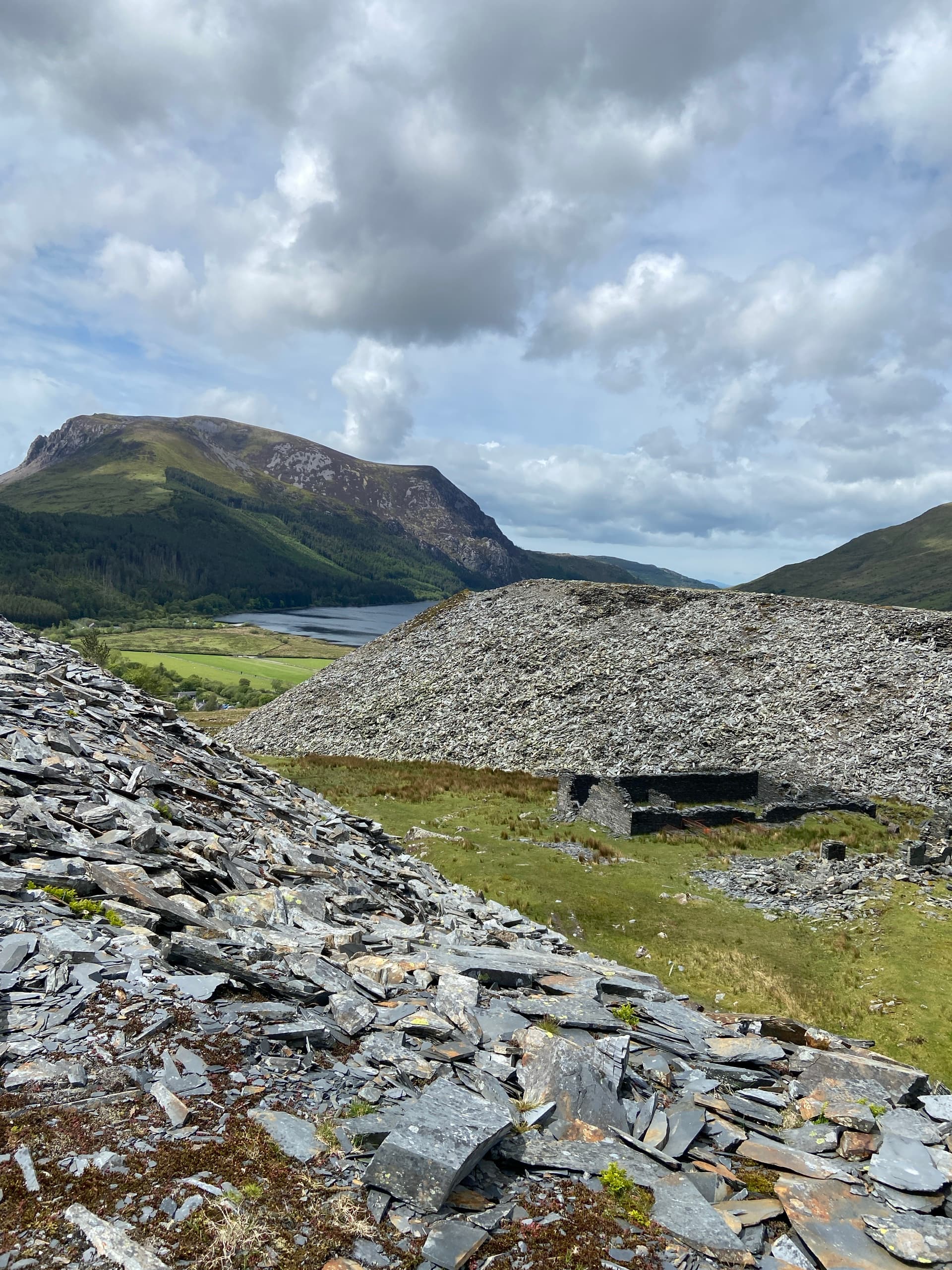 Slate tips and ruin in a mountain landscape above a valley lake under a cloudy sky
